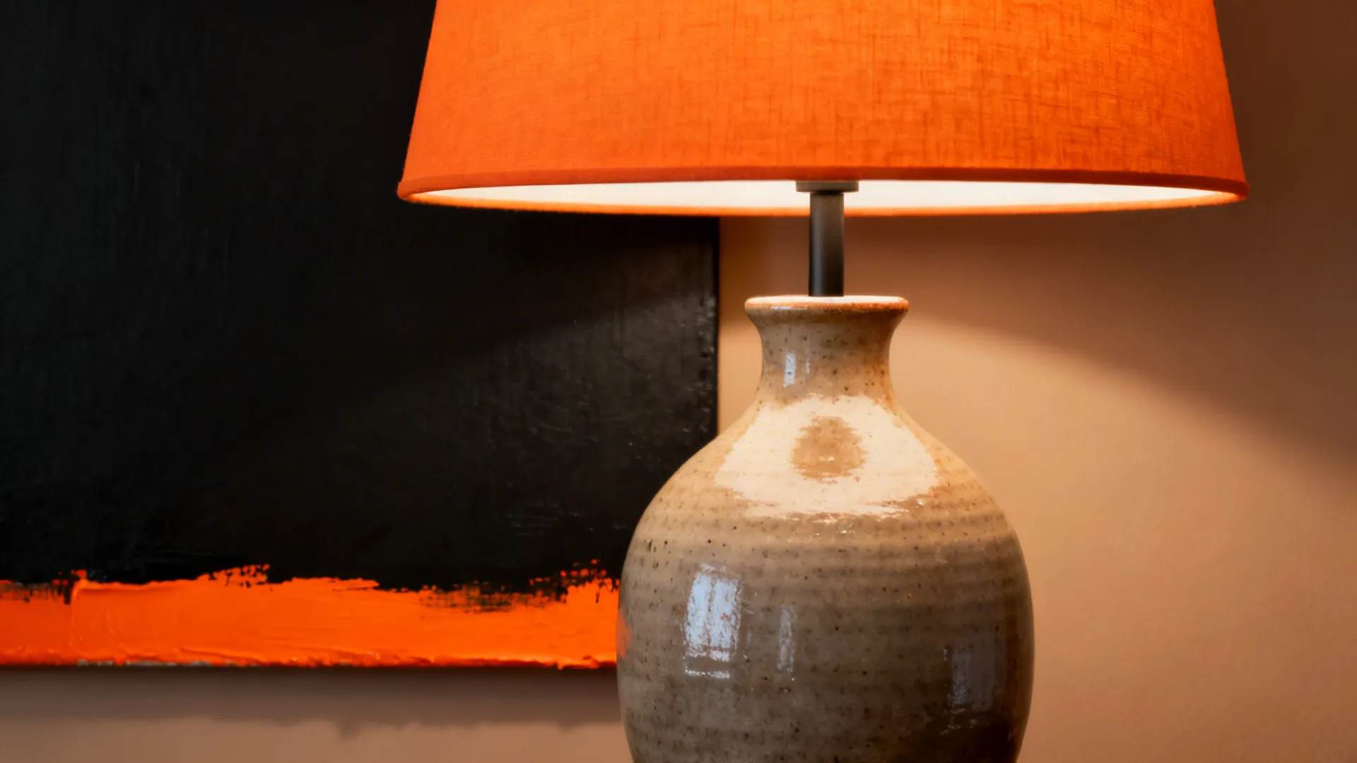 Detail of orange accents like a lampshade and vase against a monochrome background.