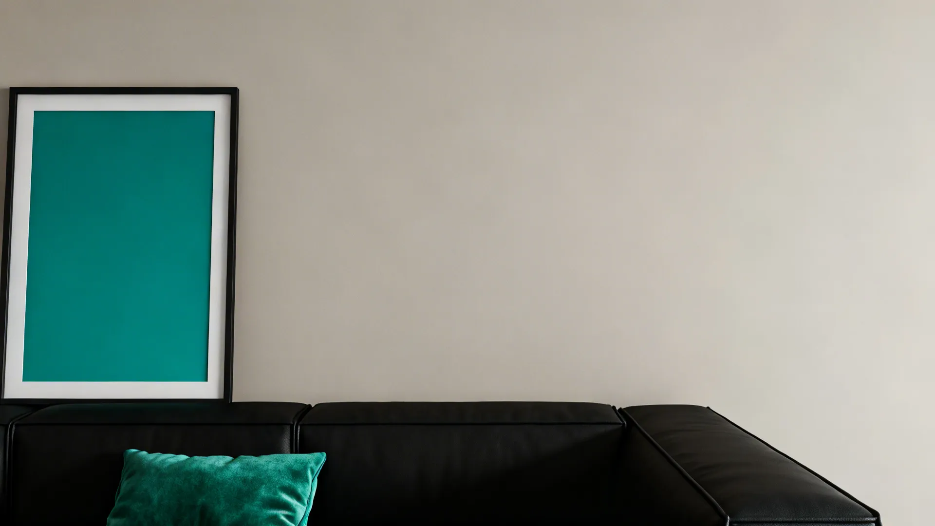 Monochrome living room anchored by black furniture with an emerald cushion and teal art as the only color pop.
