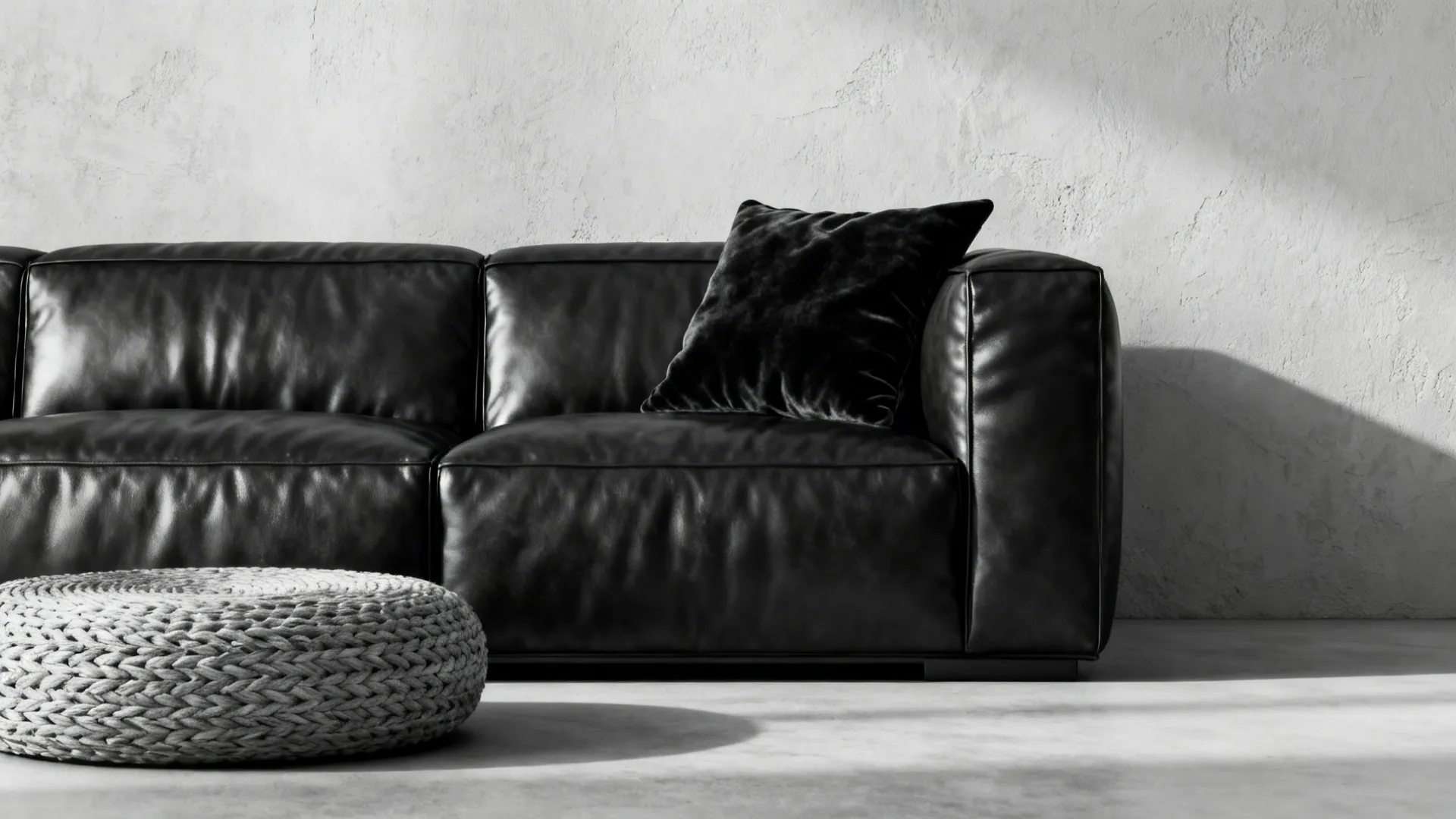 Monochrome living room with black leather sofa and varied textures like velvet and woven pouf