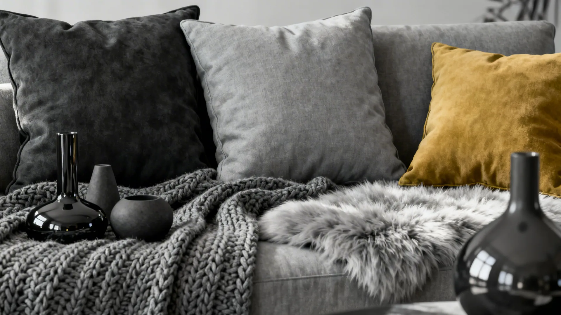 Layered monochrome cushions and textiles with a single mustard accent pillow.