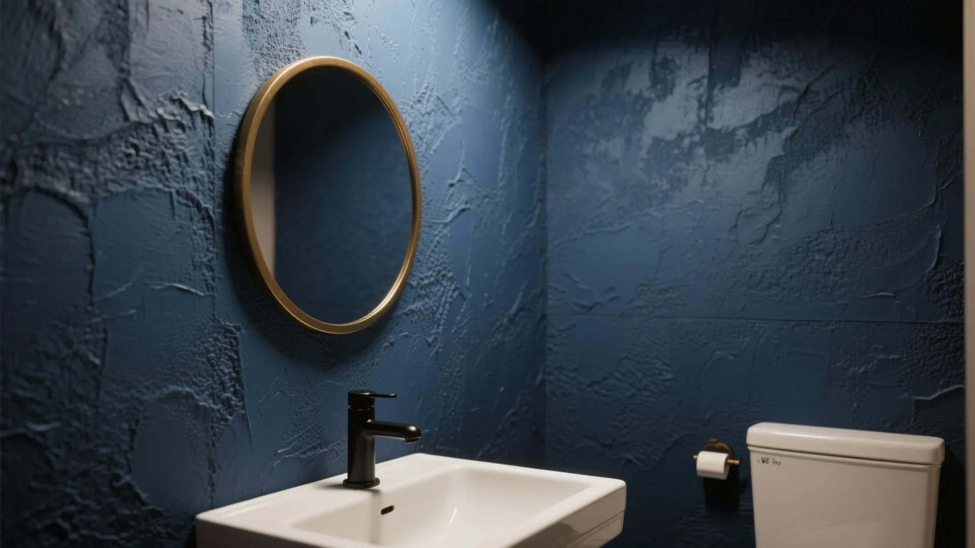 Modern bathroom with dark blue textured walls round gold mirror white sink and black faucet