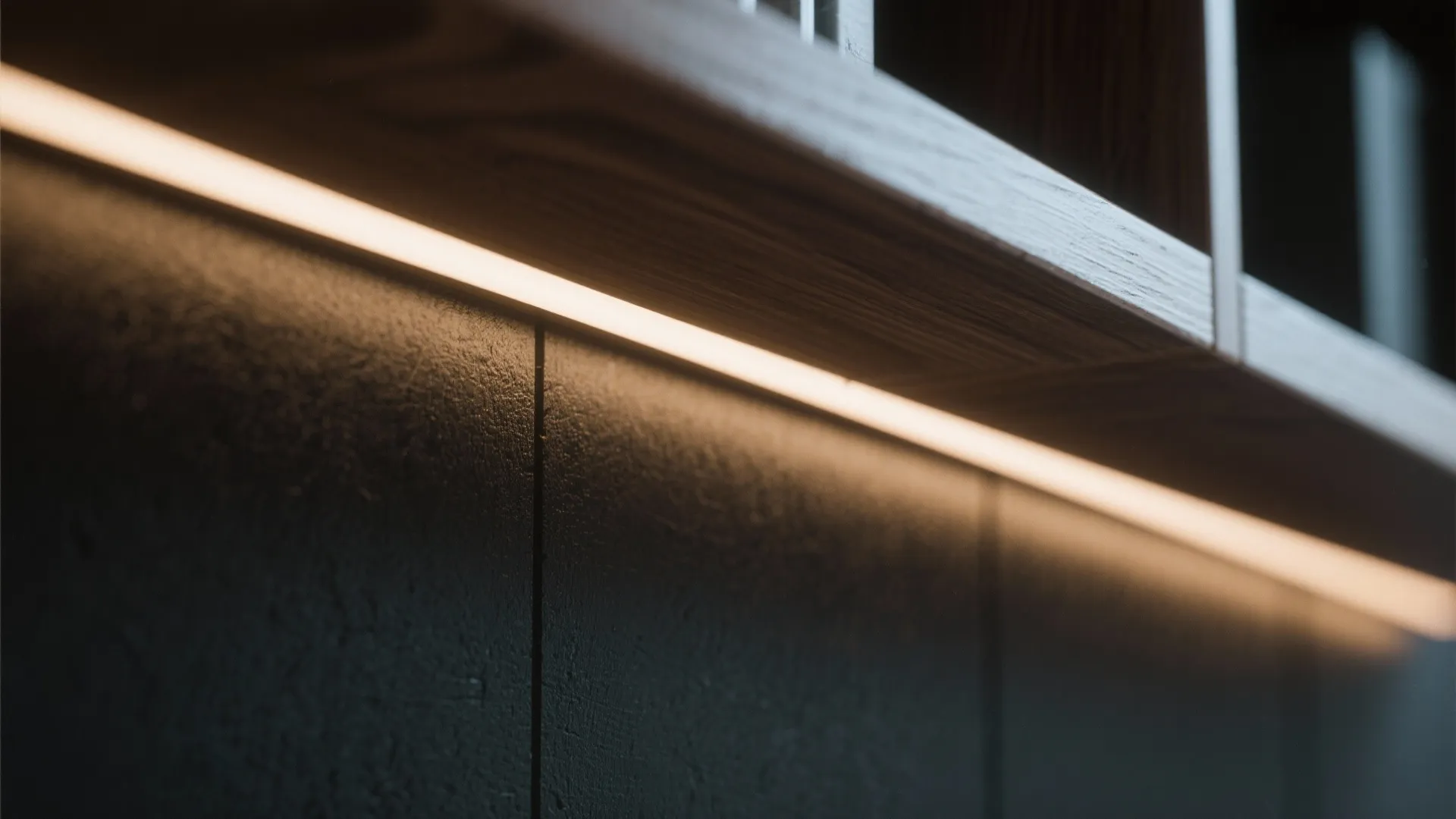 Close up of warm led light strip installed under a wooden shelf against dark wall panel