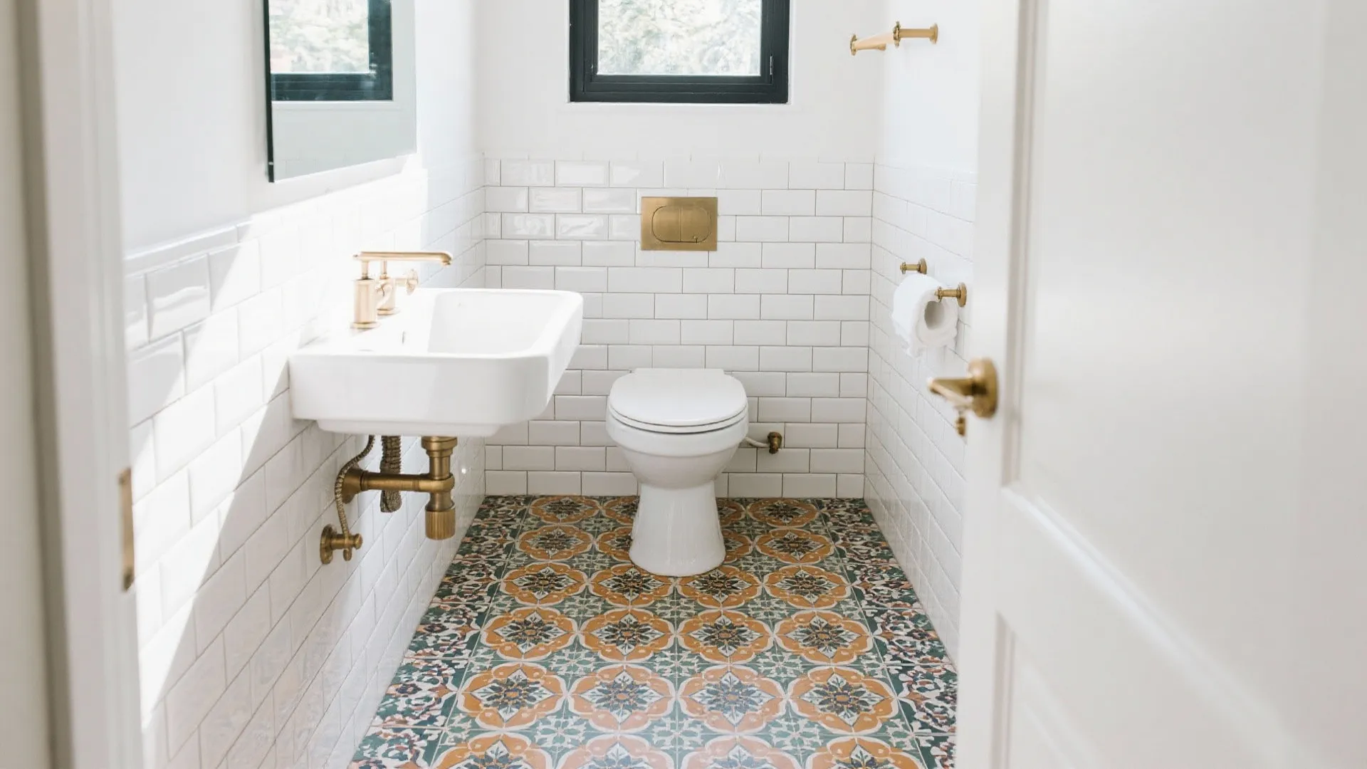 Bright bathroom with white brick wall tiles floral floor tiles gold faucet and white toilet