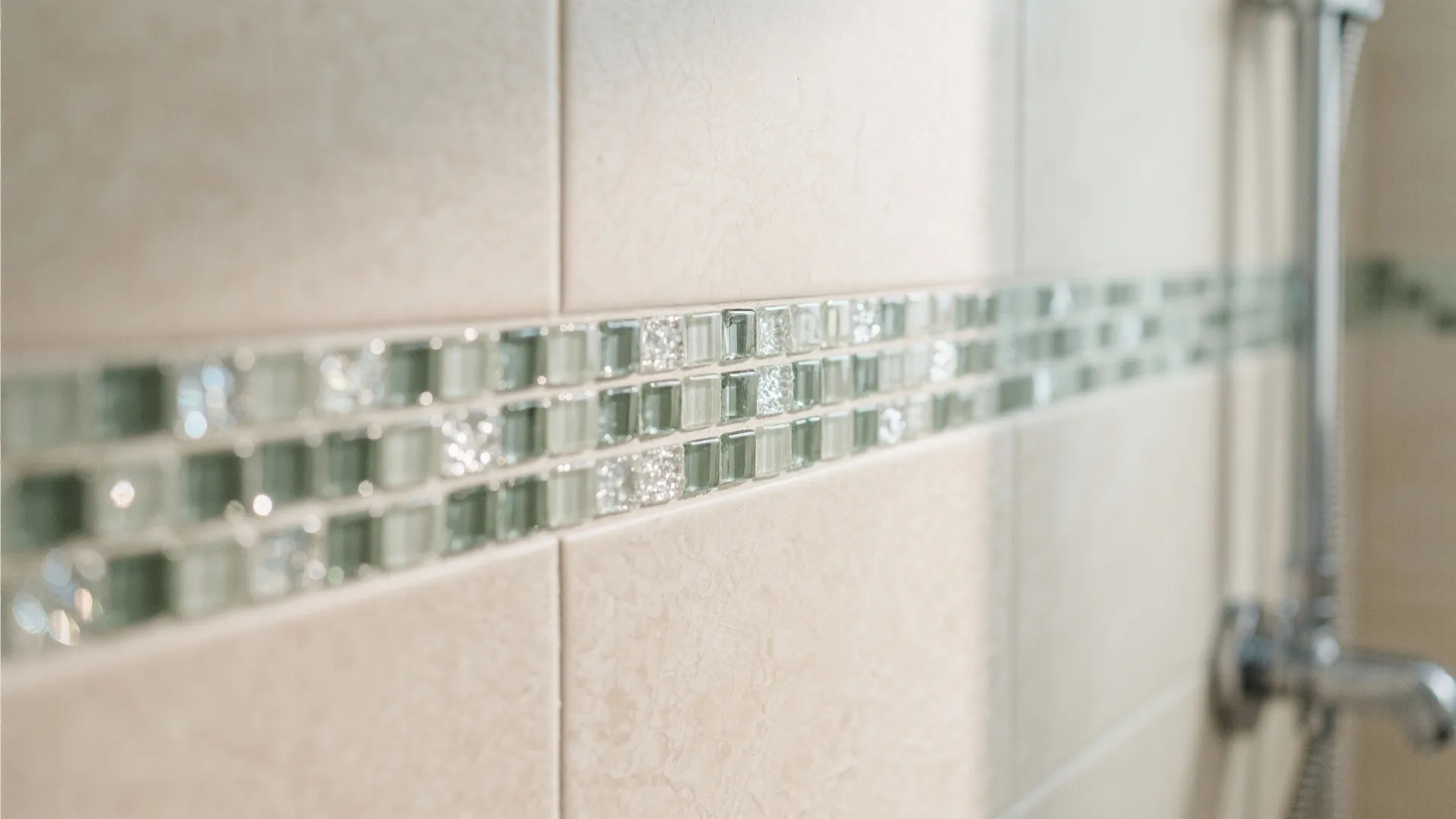 Bathroom shower area wall with a decorative horizontal band made of small green glass mosaic tiles