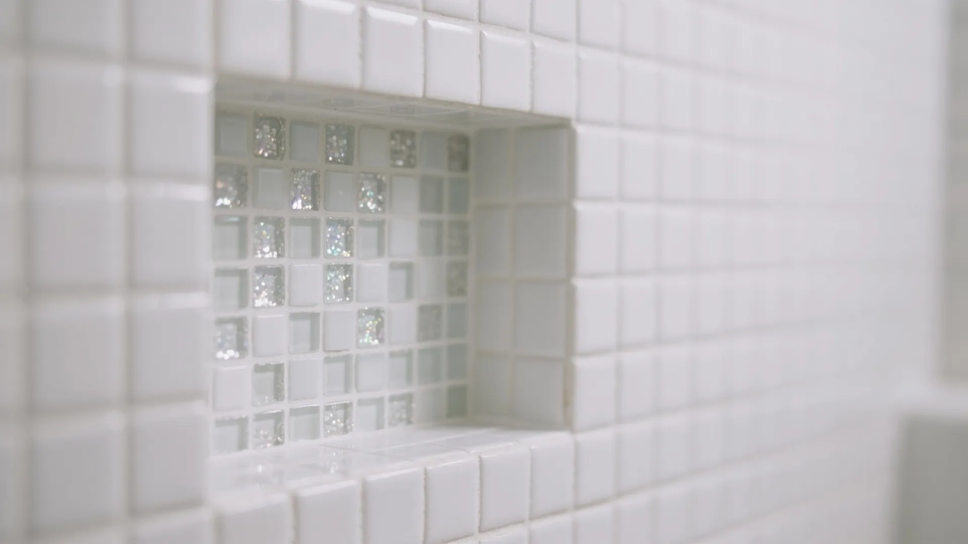 Close up of a wall shelf featuring white and shiny silver mosaic square tile design