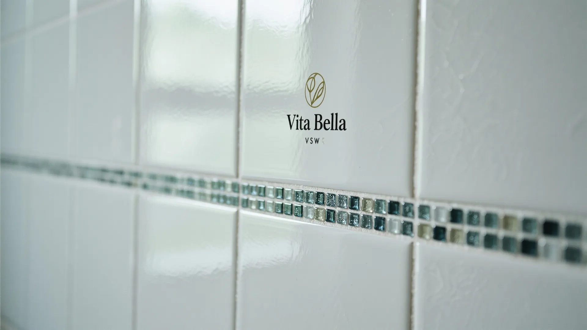 White glossy wall tiles with a small glass mosaic border and a black brand logo