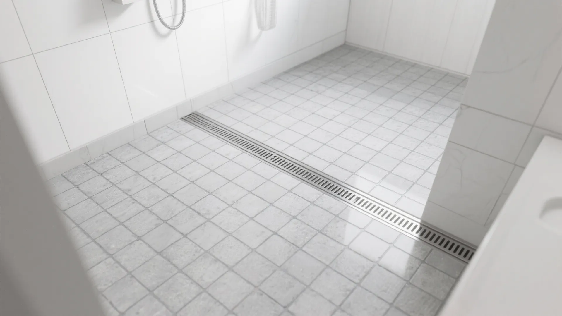 Modern white bathroom shower area with small square floor tiles and a long metal drain