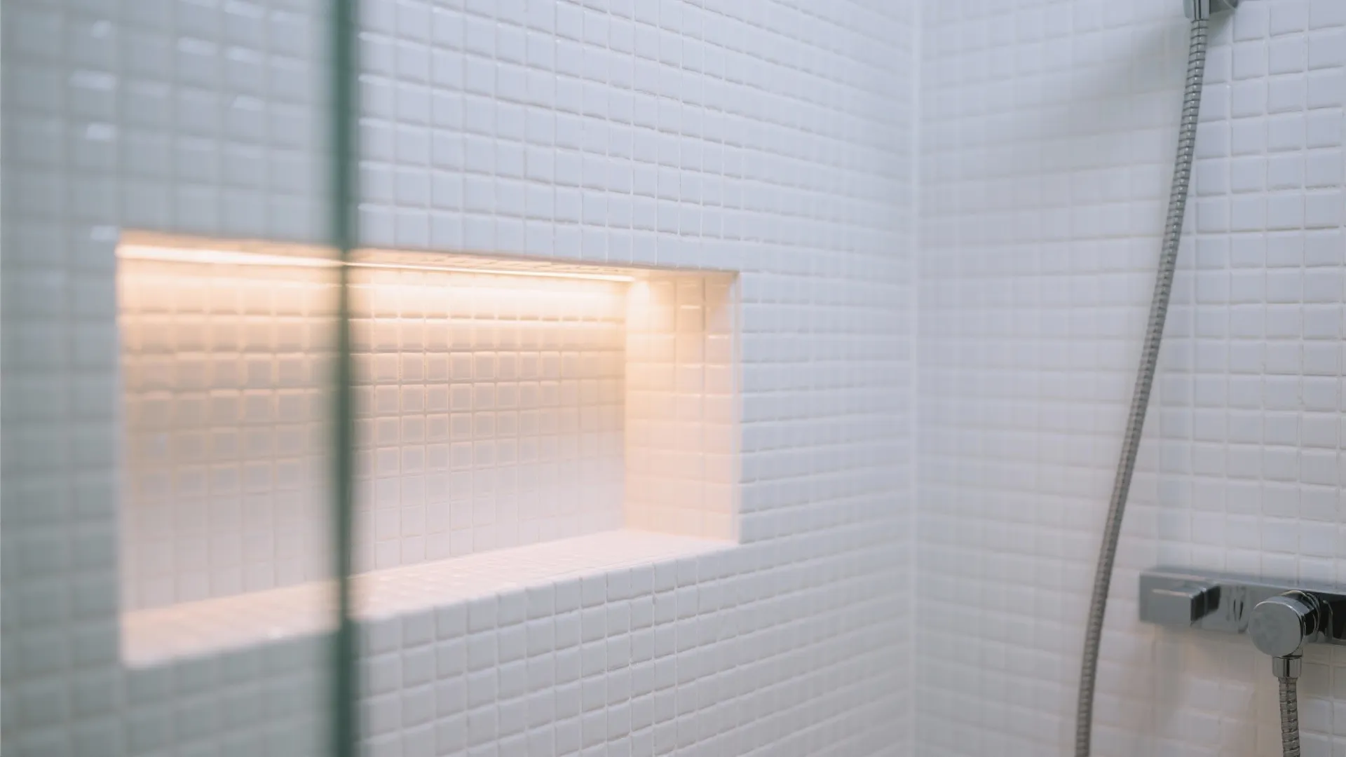 Modern shower area with white mosaic tiles and a wall shelf with built in lighting