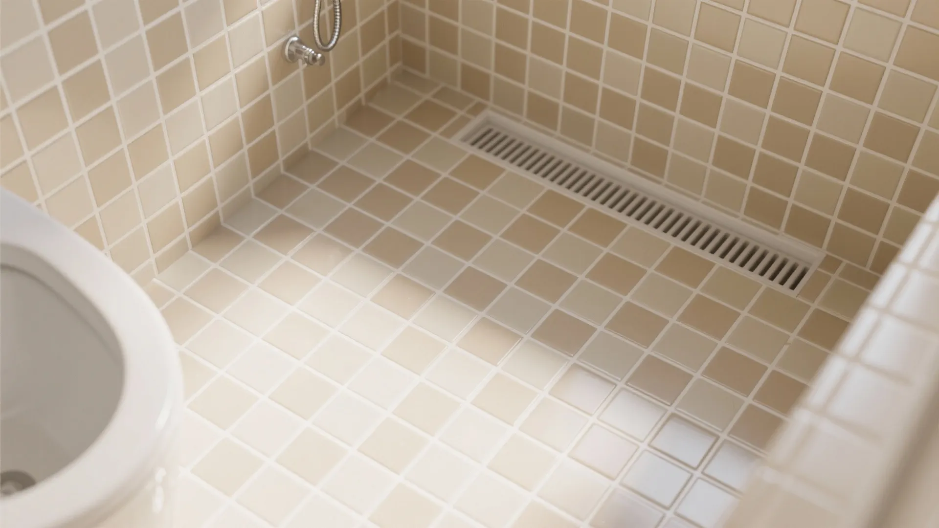 Top down view of beige square tiles on a bathroom floor with a long drain