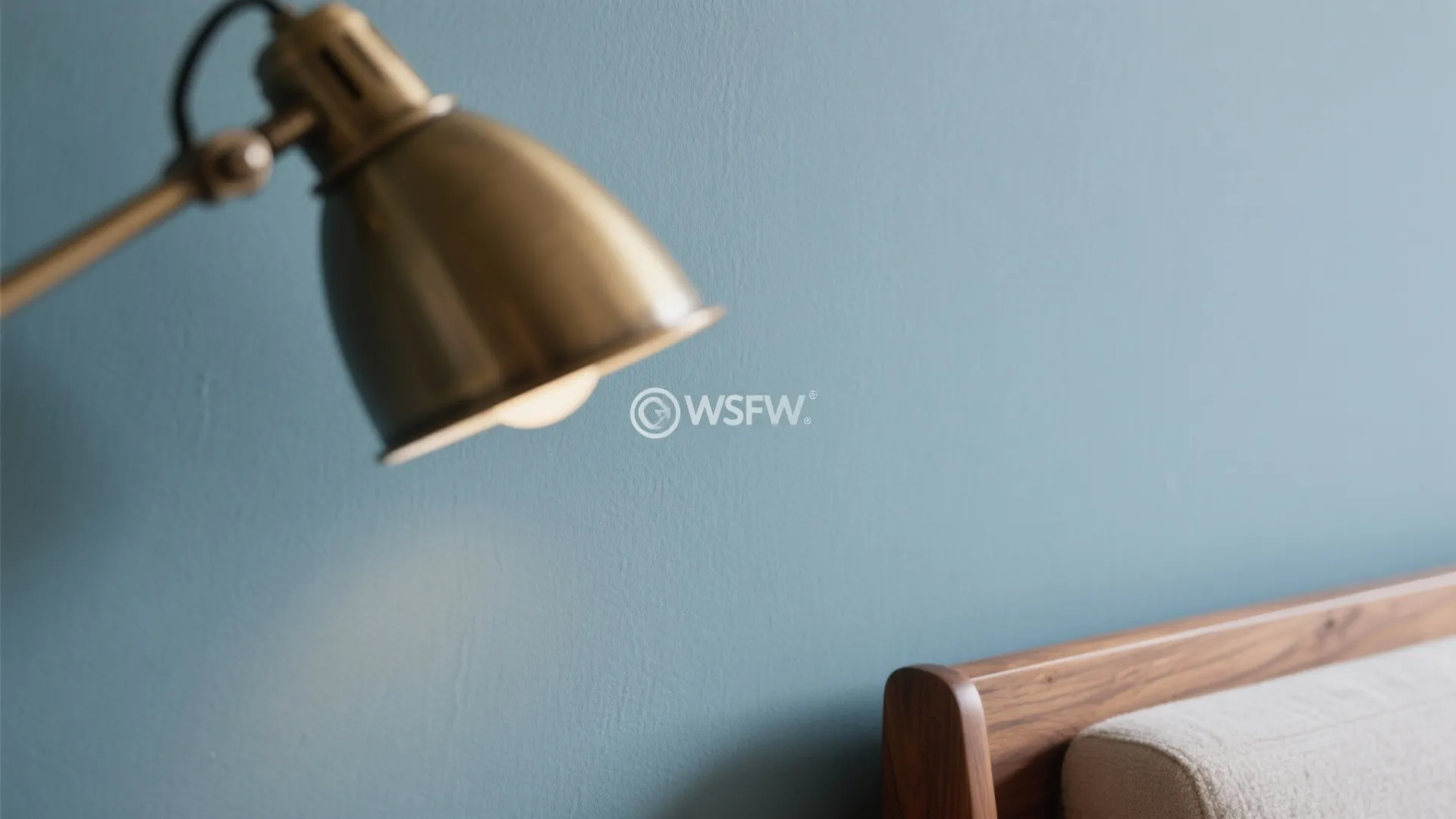 Close up of a gold wall light and wooden bed frame against a blue wall