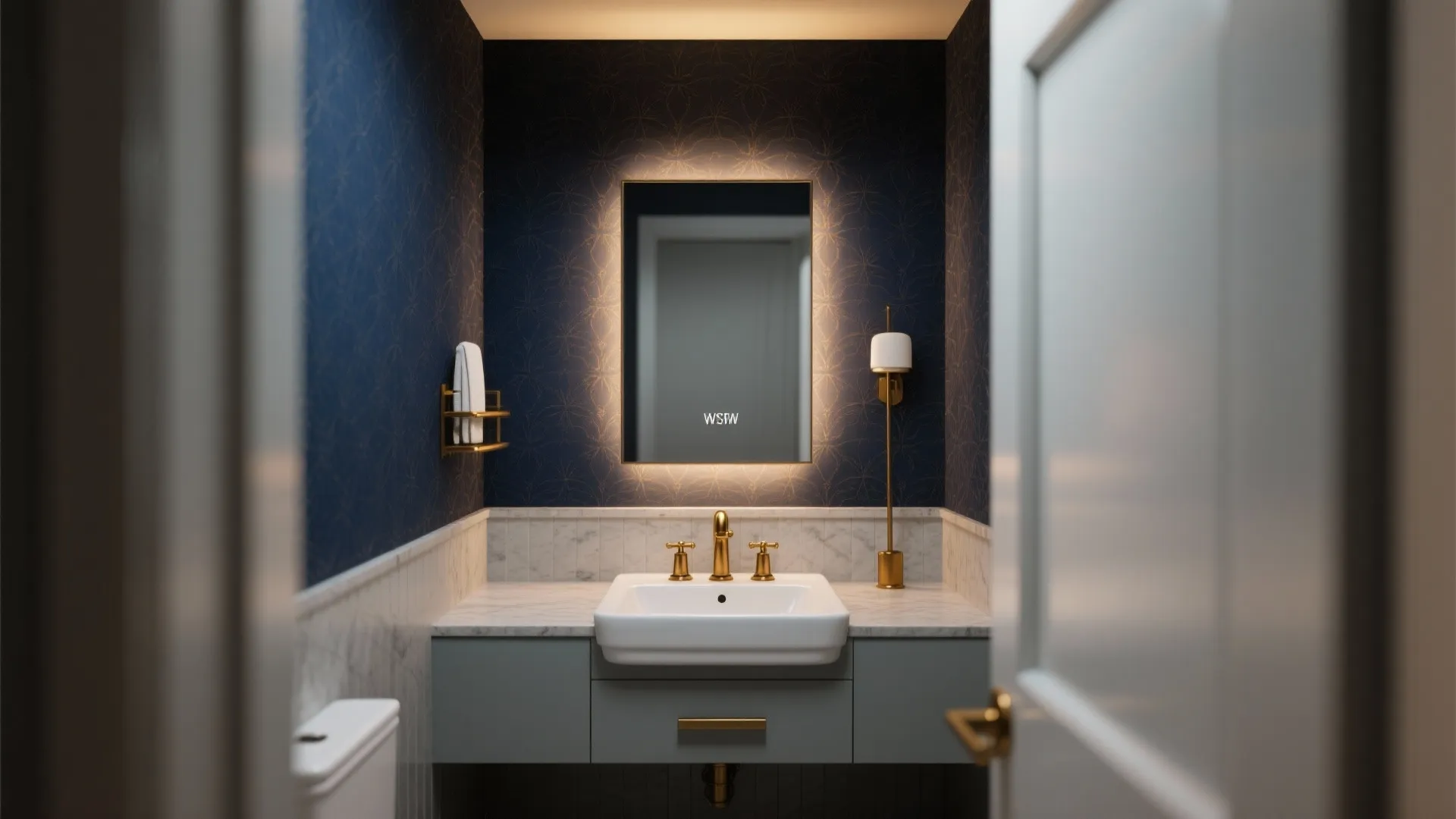 Modern bathroom featuring navy patterned wallpaper, white sink, gold faucet, lighted mirror, and grey cabinet