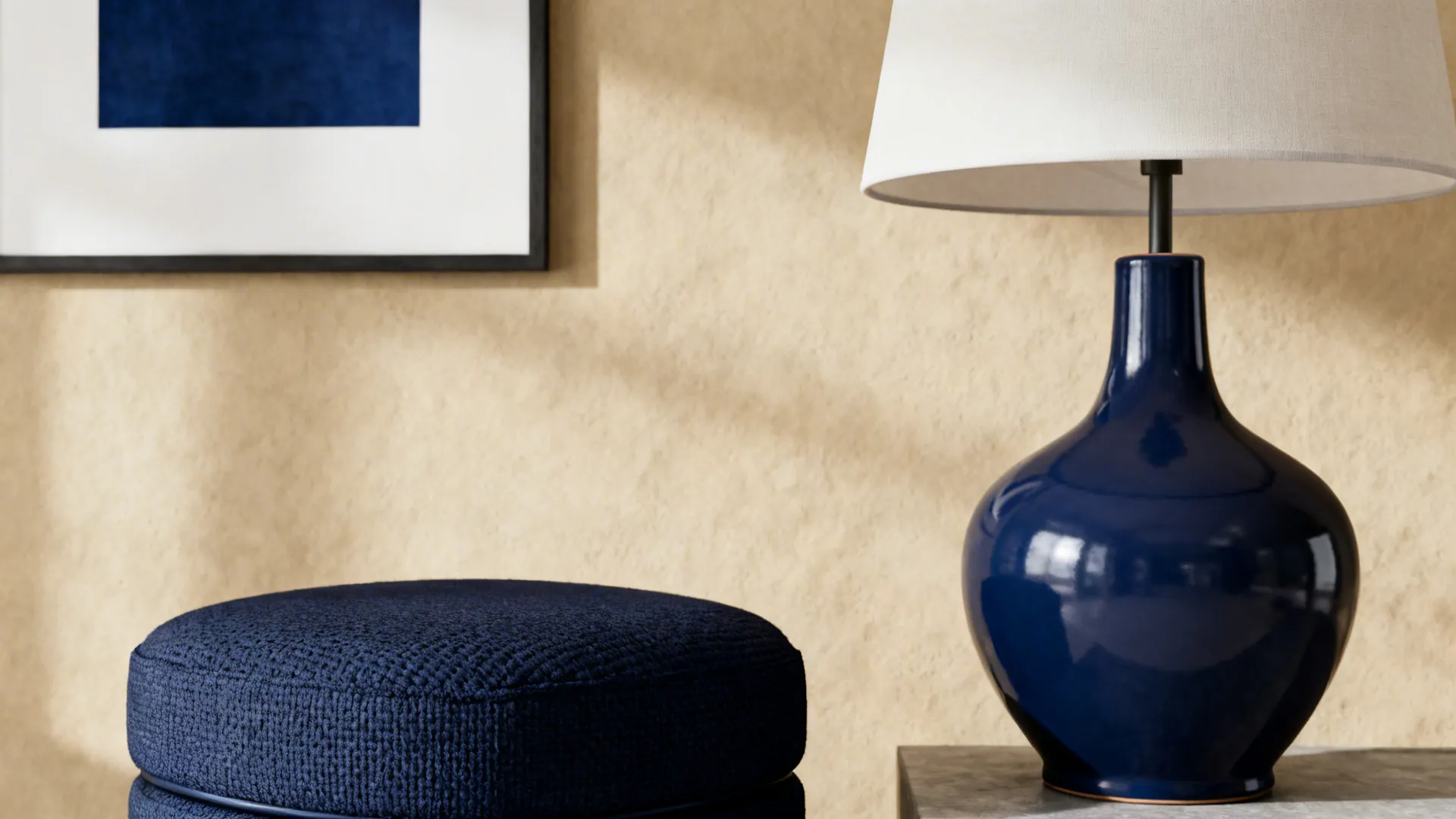 Close-up of navy ottoman, lamp and framed art as small pops against beige walls.