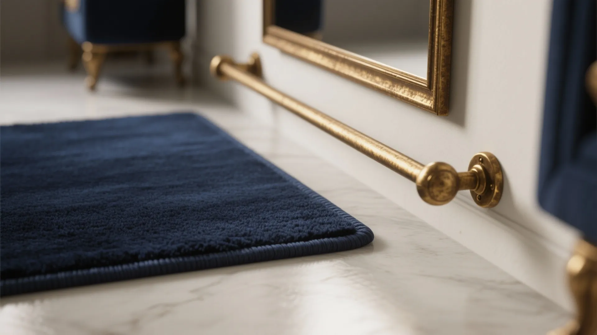 Close up of navy blue rug next to gold towel bar on white bathroom wall