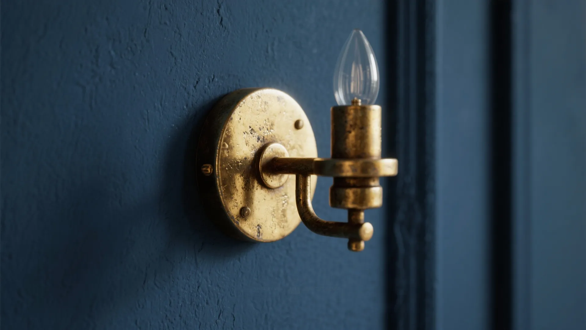 Antique brass wall light with a single bulb mounted on a dark blue textured interior wall