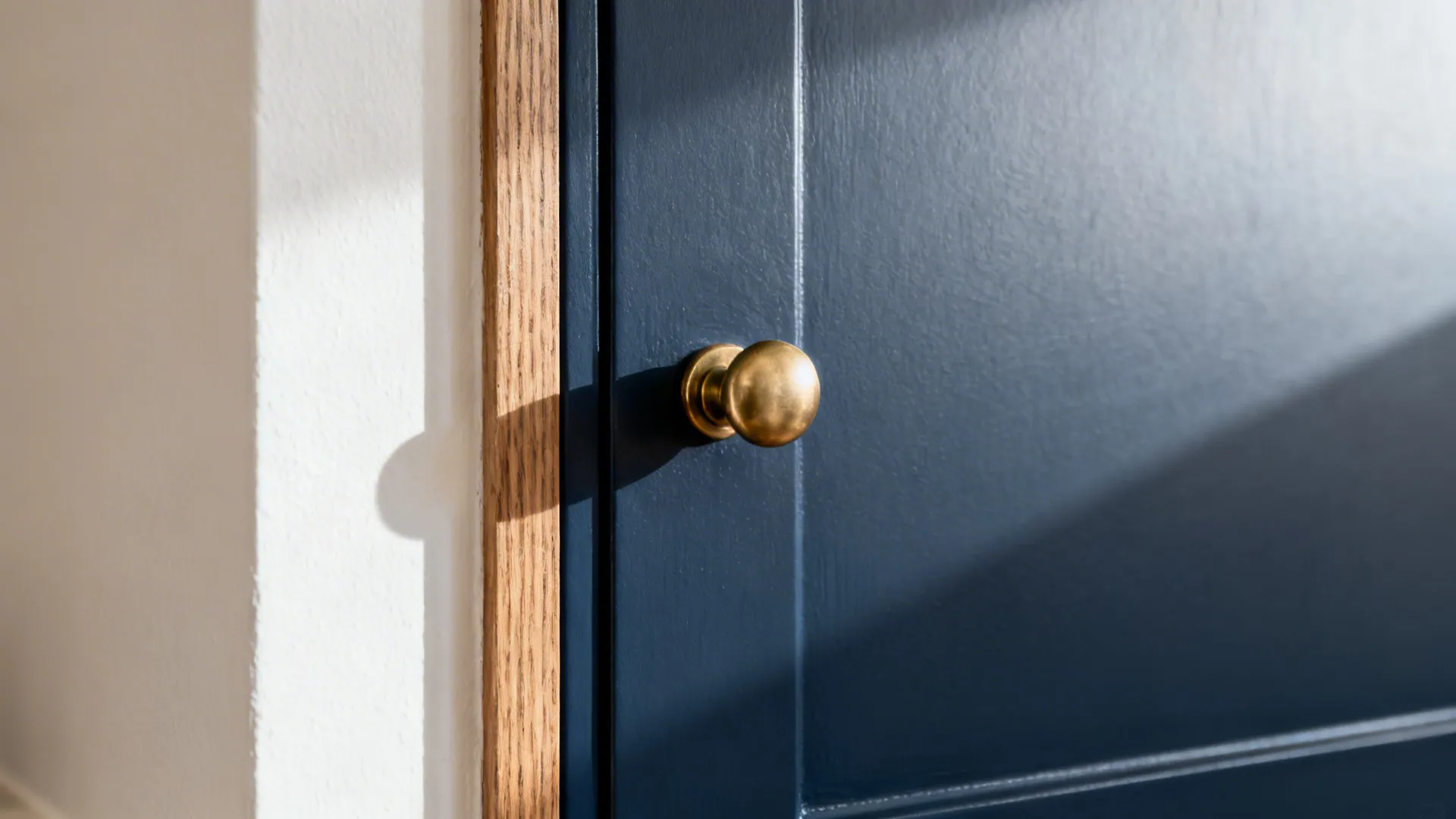 Macro of matte navy cabinet with satin brass pull beside warm white wall.
