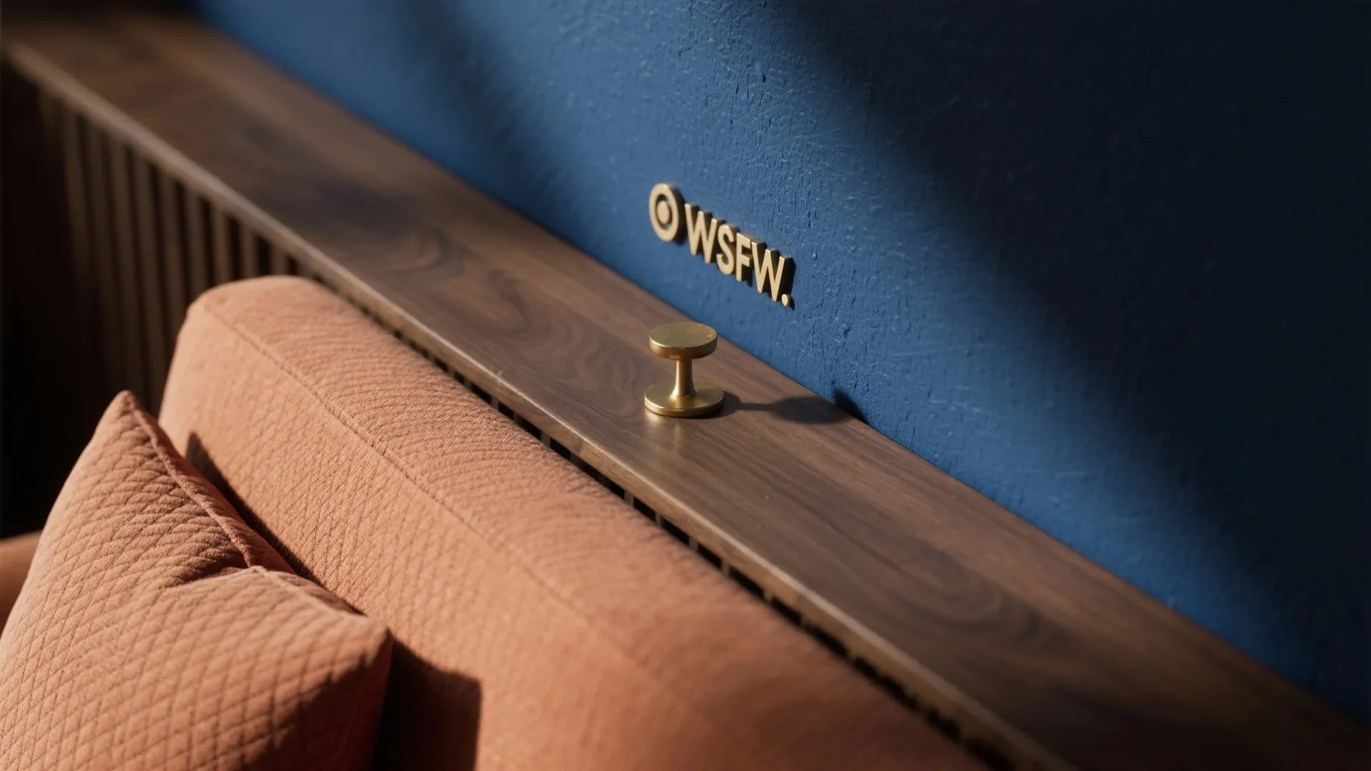 Blue wall with gold logo above a wooden shelf next to a textured orange pillow