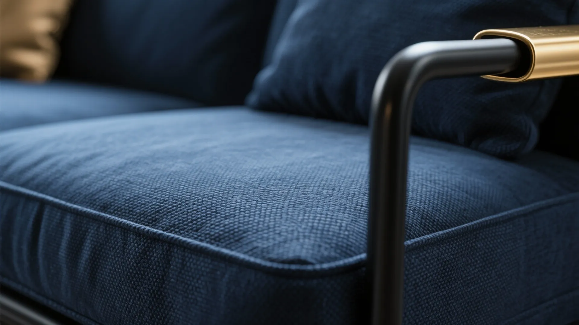 Detailed view of navy blue fabric sofa cushion with a black and gold metal armrest