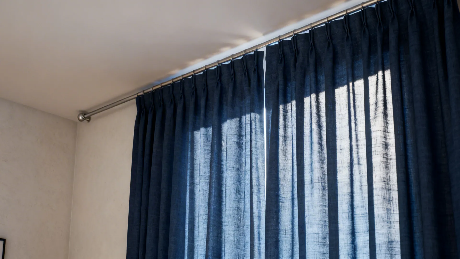 Navy blue curtains hanging from a metal rod on a white wall with bright sunlight