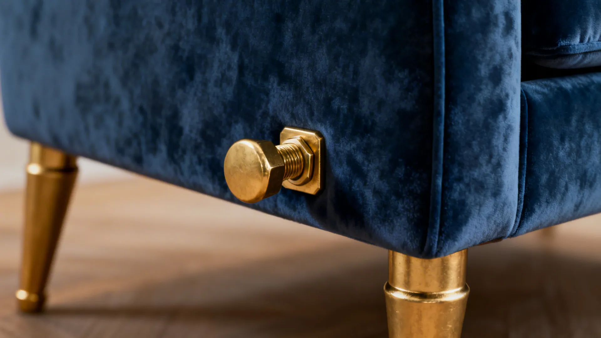 Close-up of navy velvet sofa leg and gold hardware showing texture and warm metallic finish.