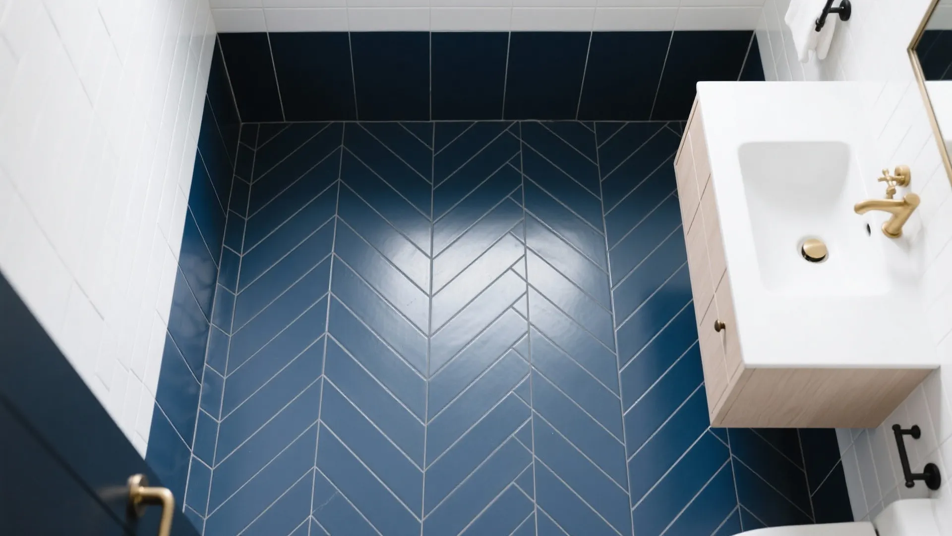 Top view of blue herringbone floor tiles in a bathroom with white sink and gold faucet