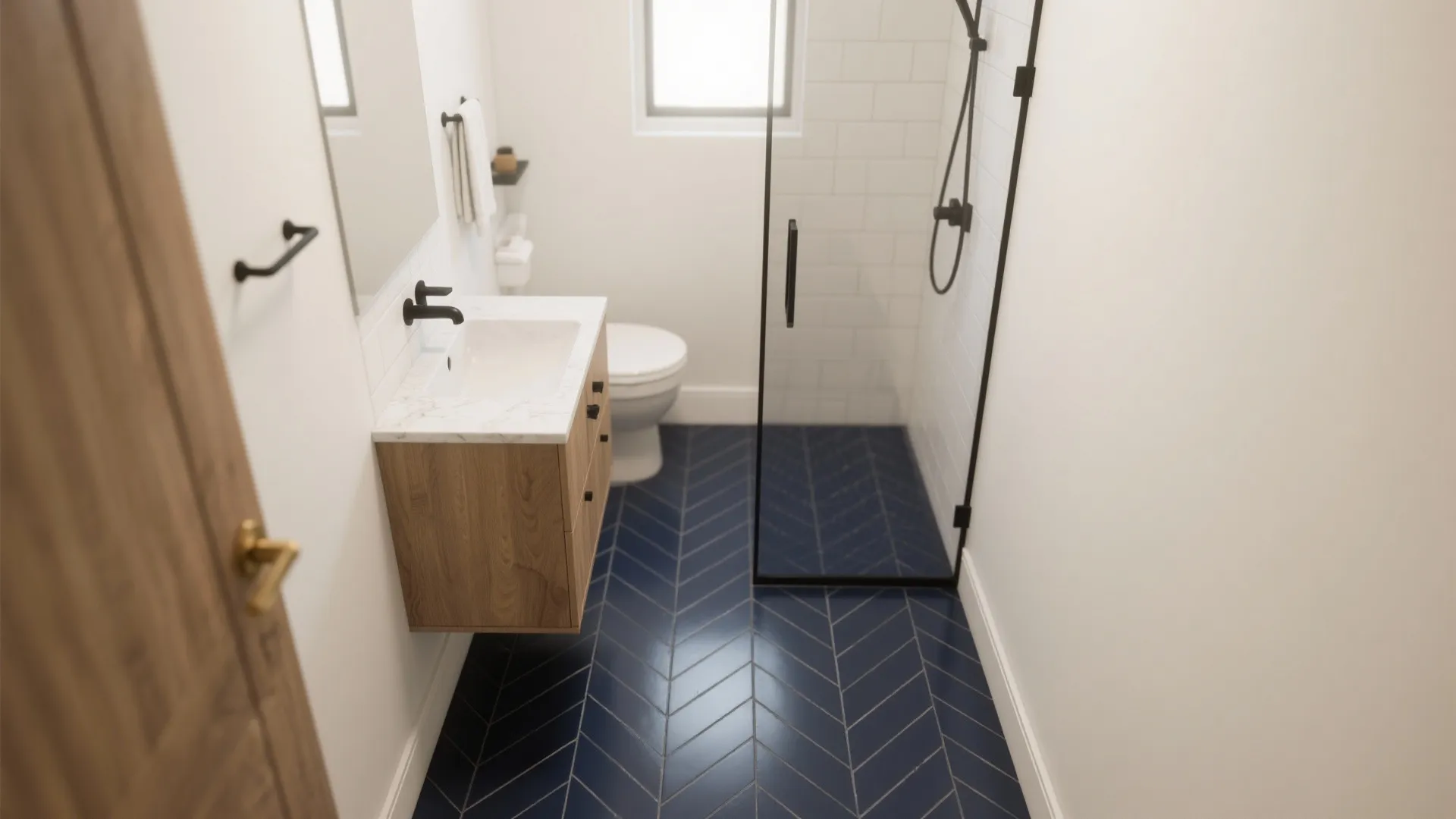 Deep navy porcelain herringbone floor in a compact bath with pale walls and light oak vanity, narrow charcoal grout, soft daylight.