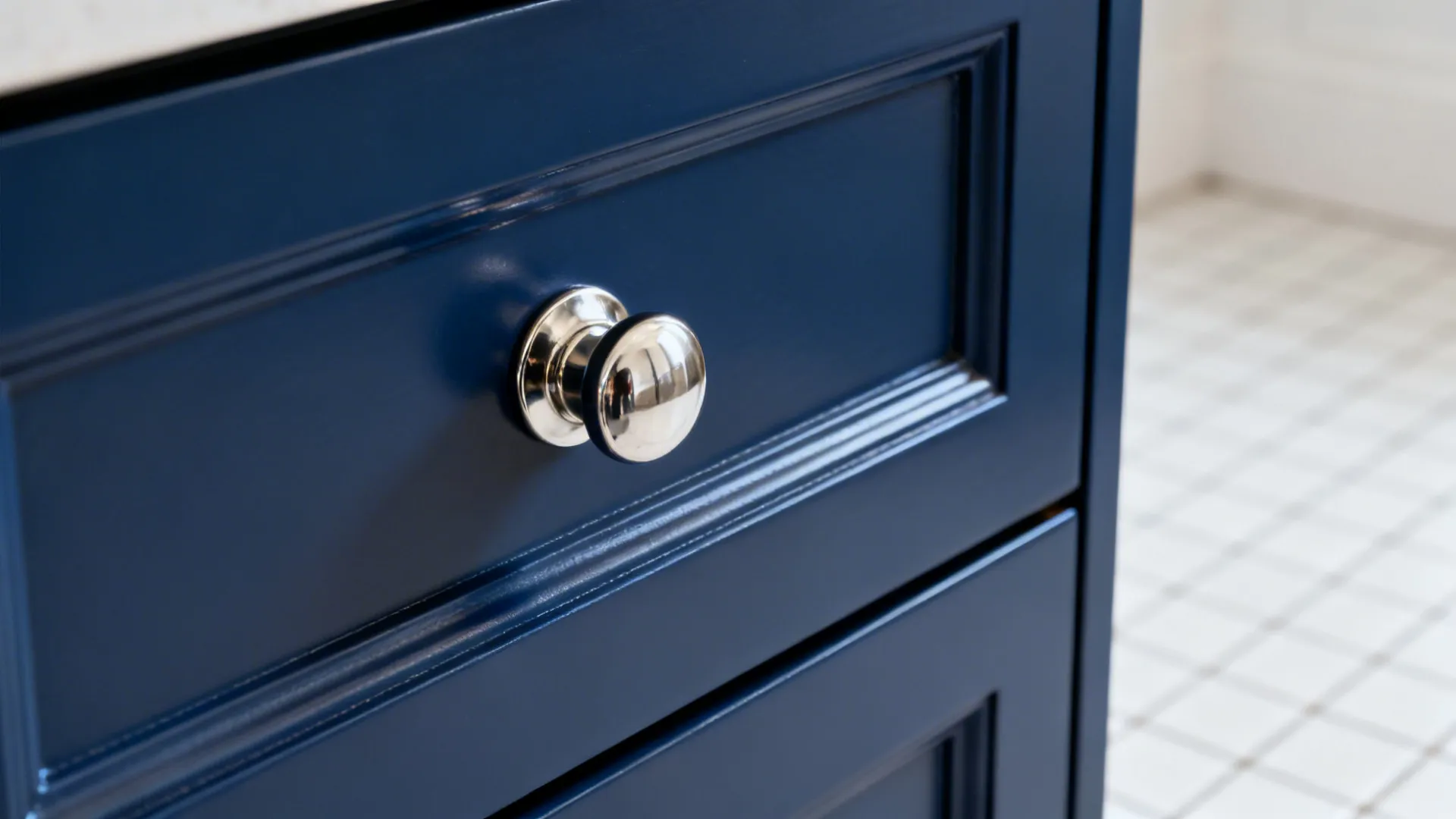Close up of a silver metal knob attached to a navy blue kitchen cabinet drawer