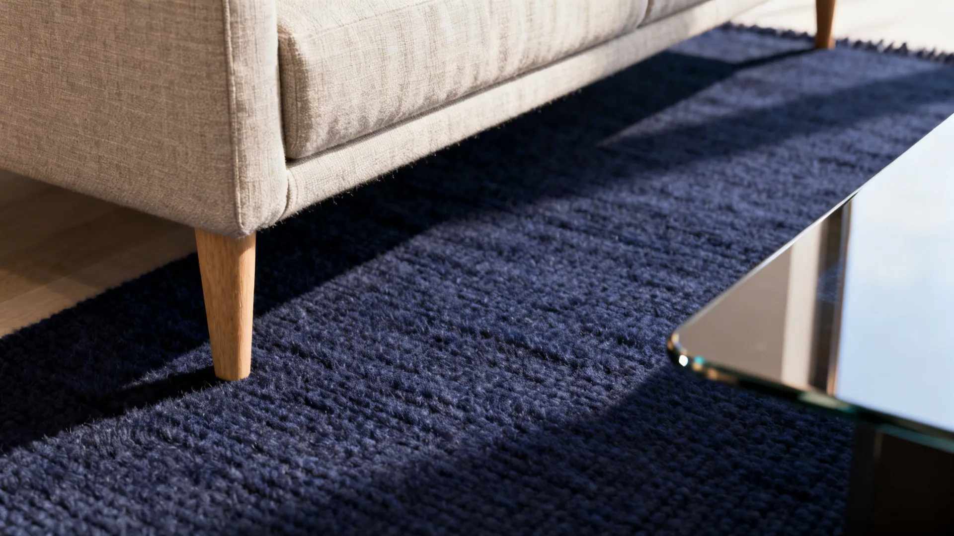Macro view of a deep navy wool rug texture beneath sofa leg and coffee table.
