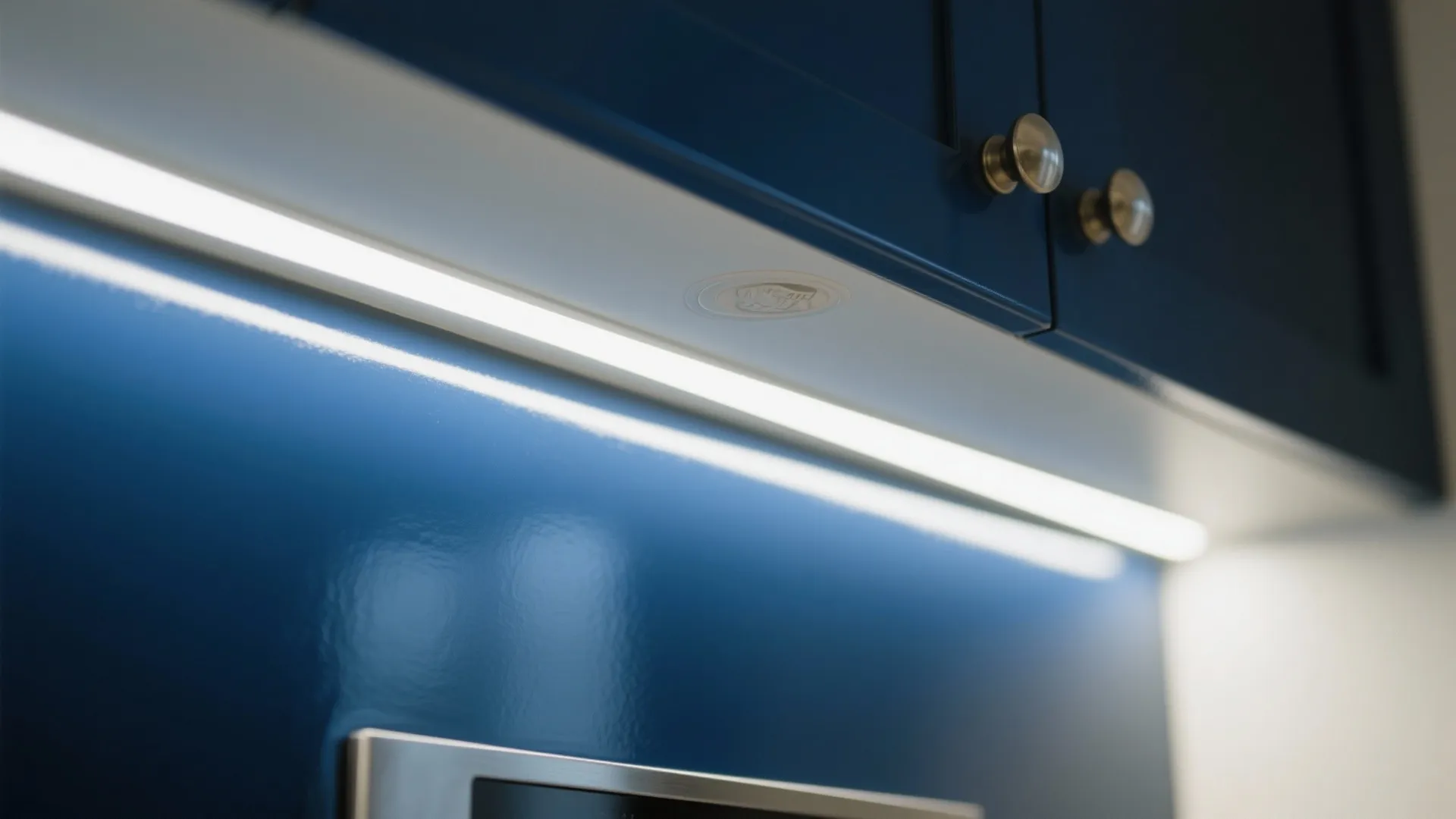 Blue kitchen cabinet with bright white light strip underneath and small gold knobs for modern look
