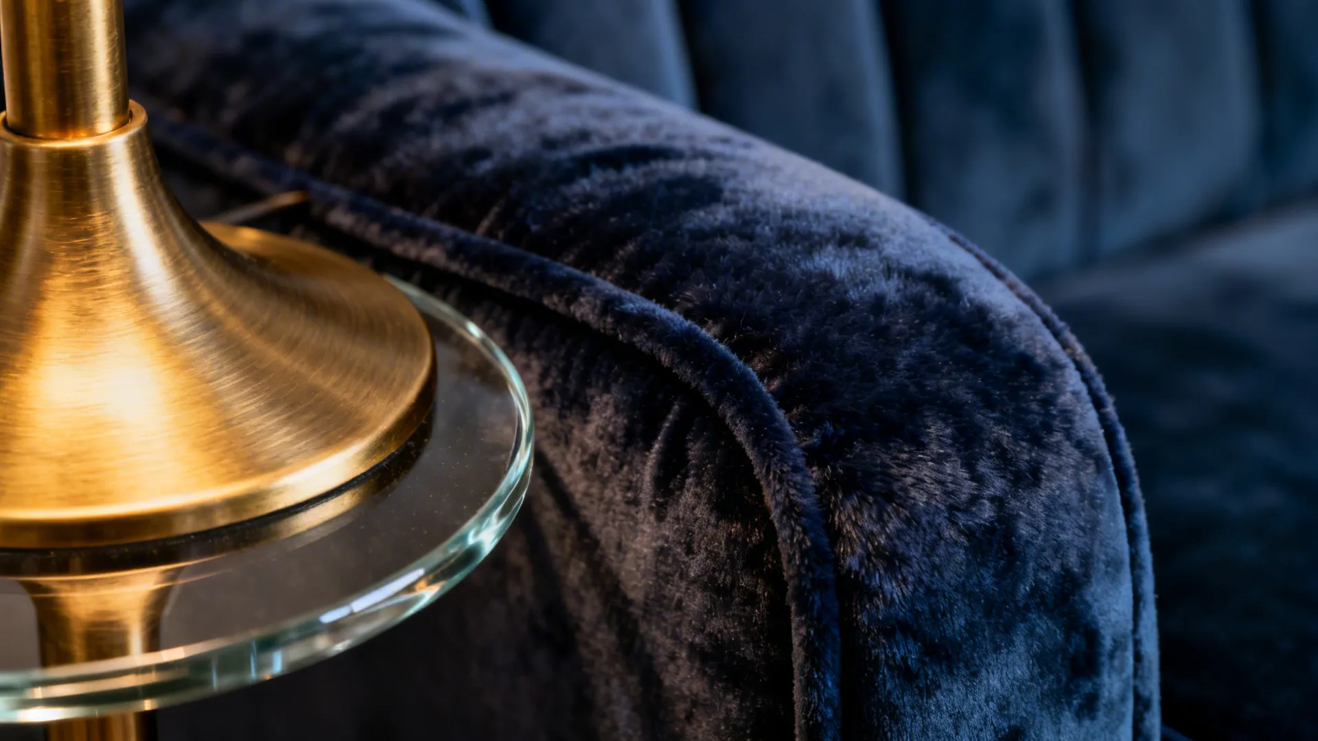 Macro of navy velvet upholstery beside a brushed brass lamp and glass edge.