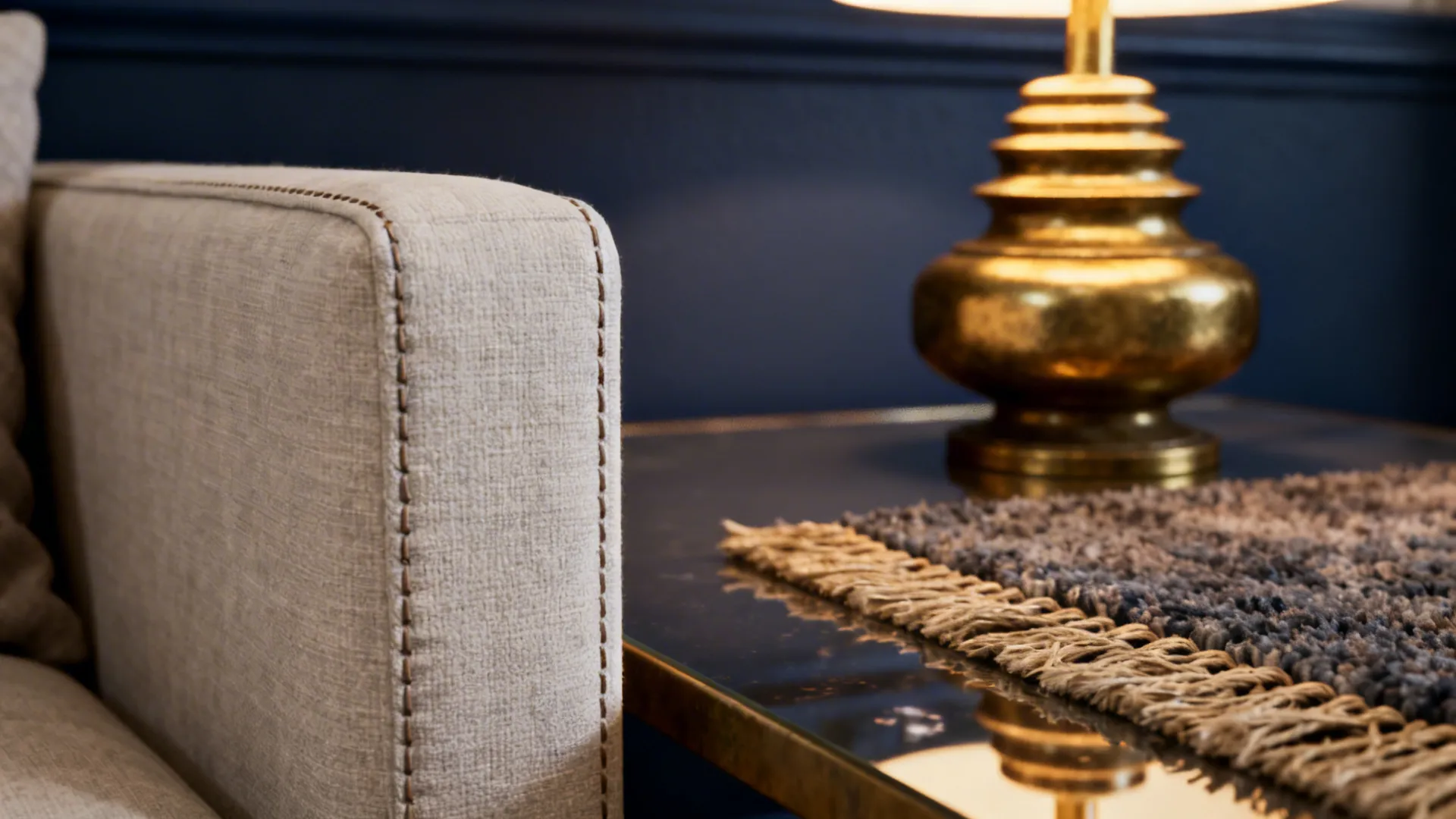 Beige sofa arm next to a gold table light fixture against a dark blue wall