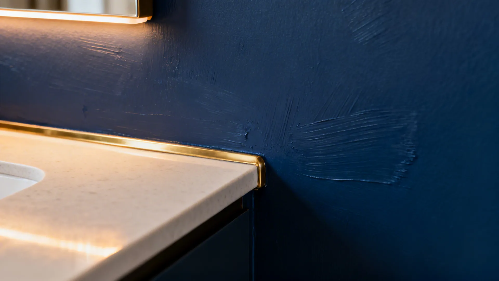 Textured navy blue wall paint next to white stone countertop with gold trim and light