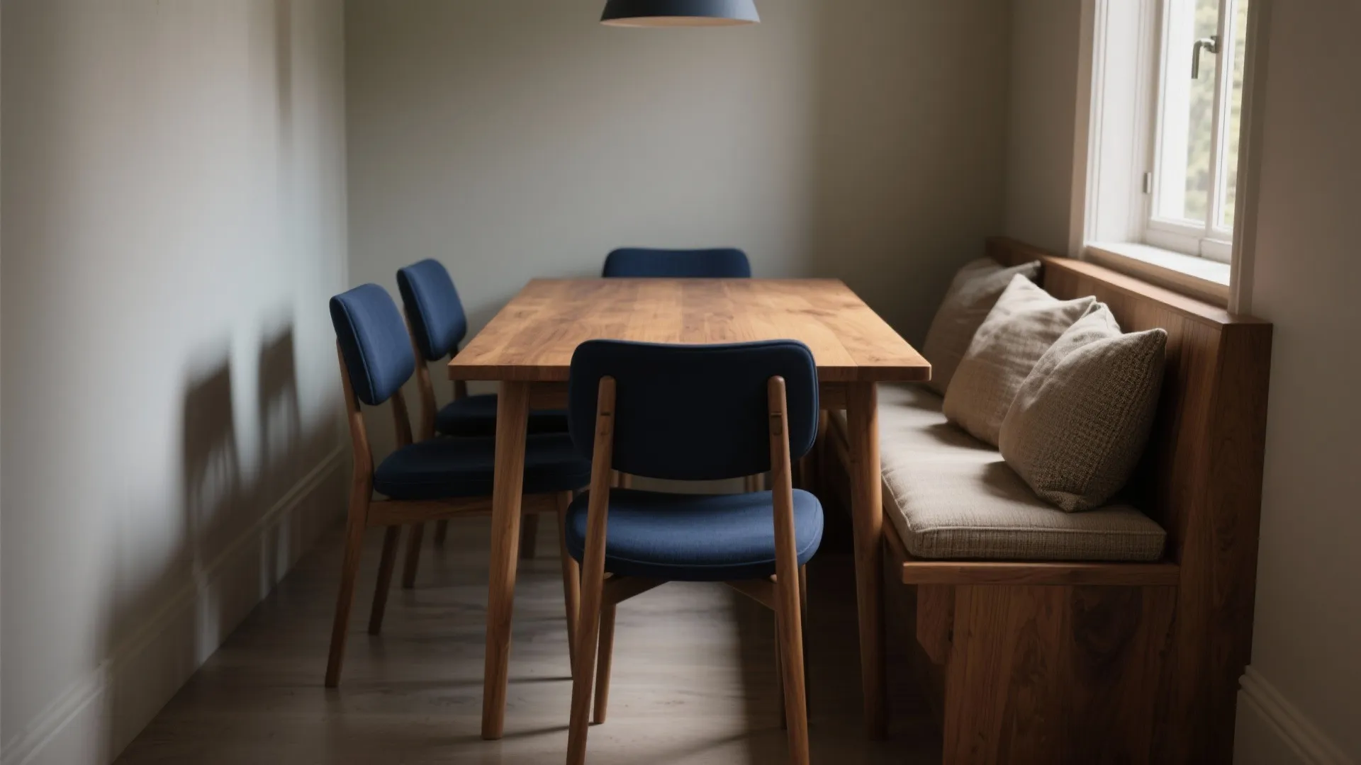 Wooden dining table with navy blue chairs and built-in bench seating under a black light