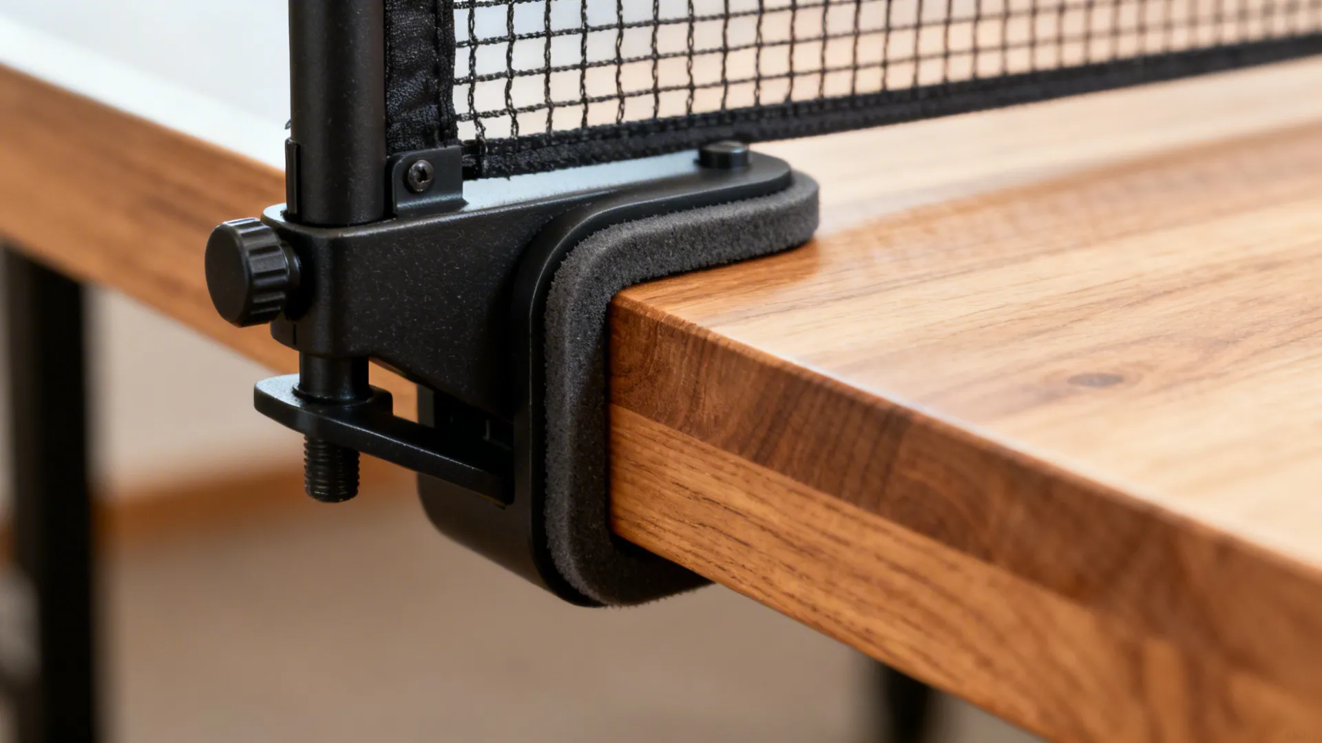 Close-up of a retractable net clamp with rubber pad protecting a wood table edge
