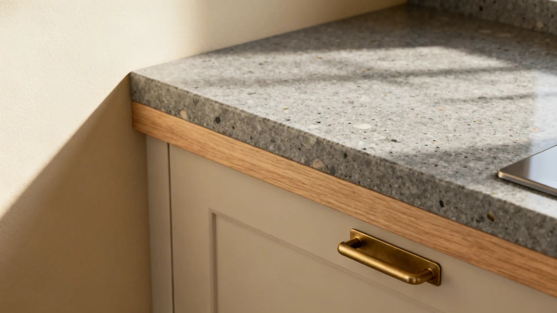 Macro of creamy sand wall, honed grey quartz, light oak, and matte brass pull in soft light.