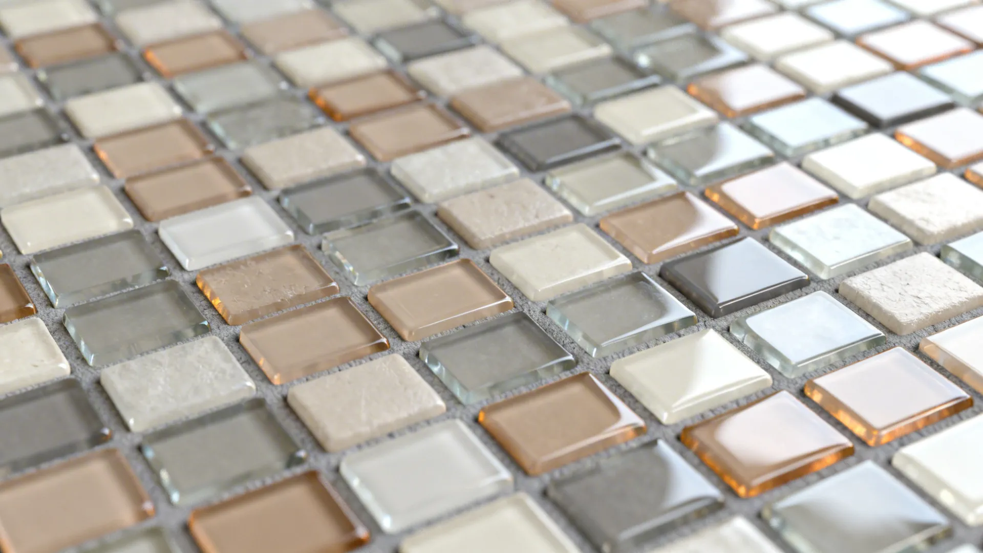 Macro of glossy neutral glass mosaic tiles with warm gray grout joints.