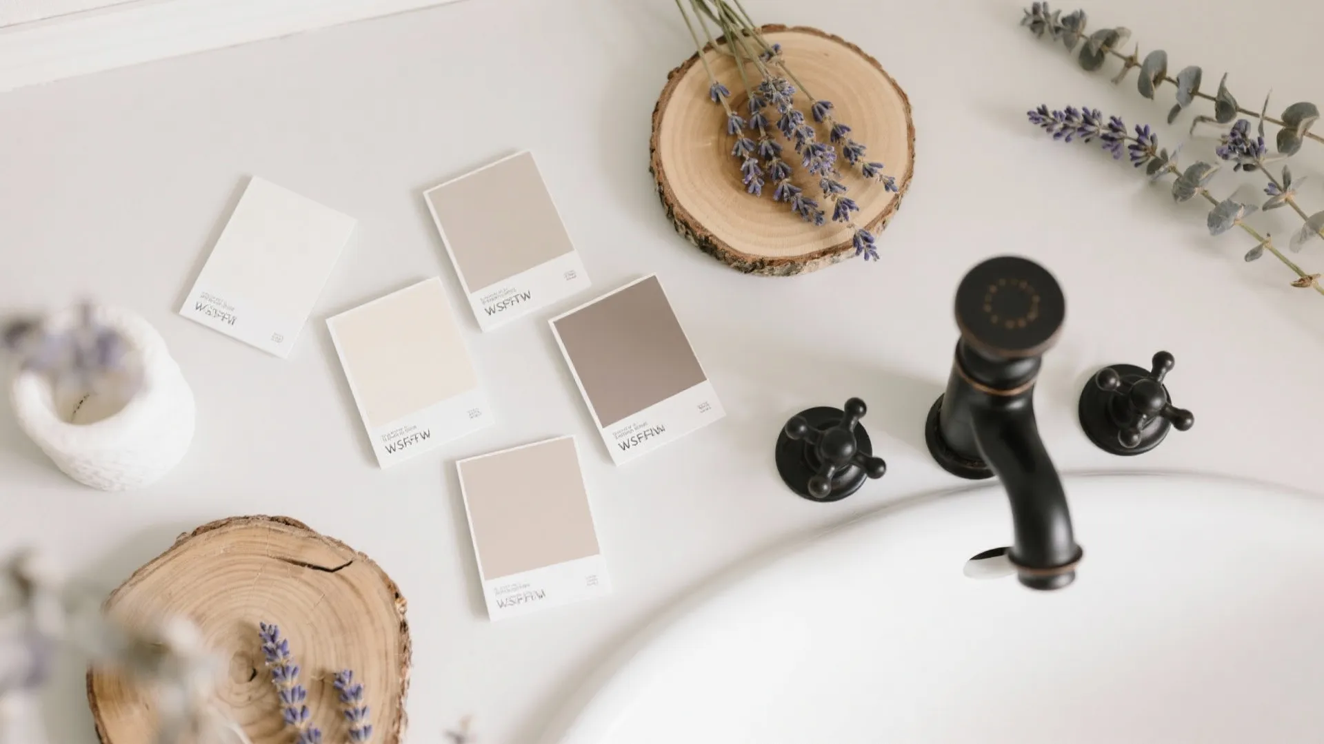 Neutral color paint samples on a white bathroom counter next to black sink water tap