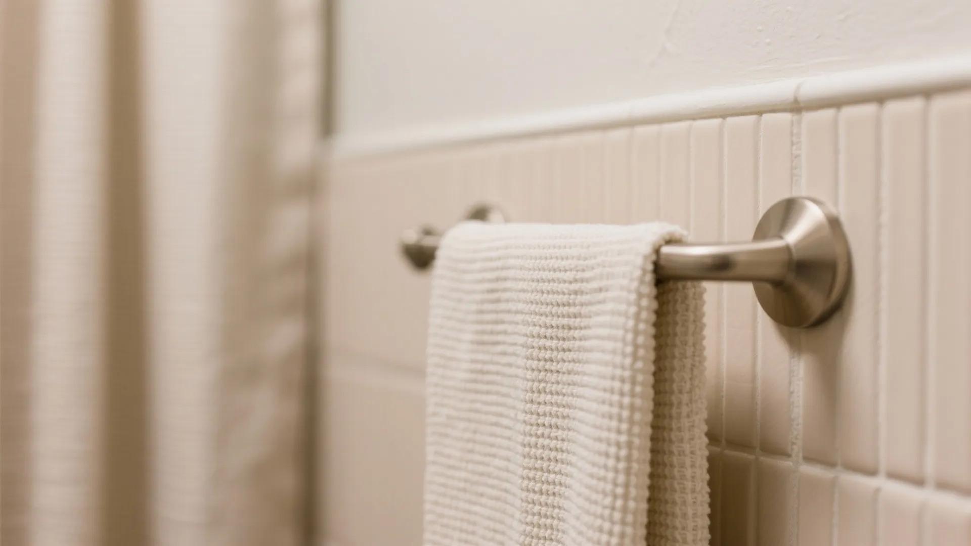 Macro of greige satin paint, matte almond tile, linen curtain, and brushed nickel hook.