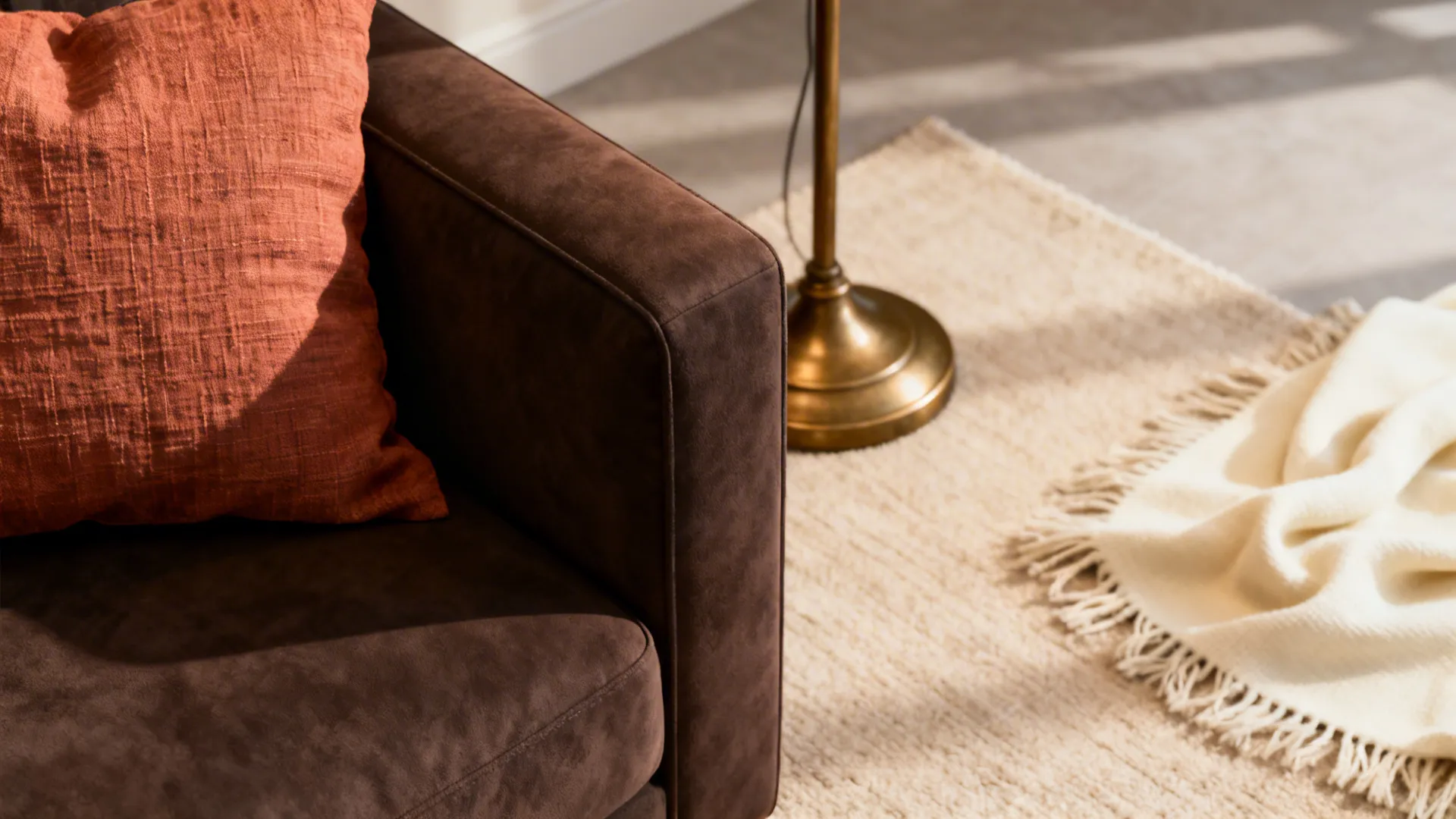 Close-up of terracotta cushion, brass lamp and cream throw on a dark brown sofa.