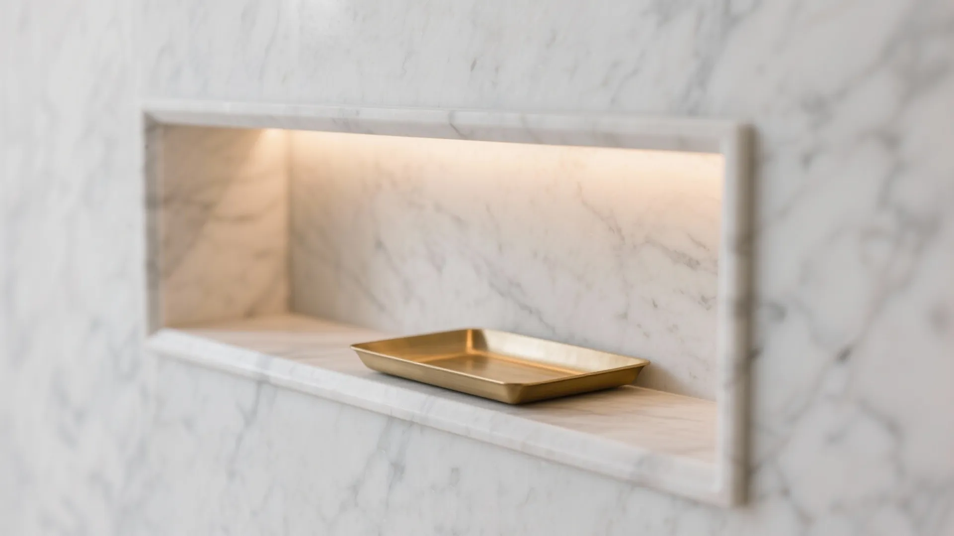 Close-up of honed white marble niche edge with brushed brass shelf and warm LED glow.