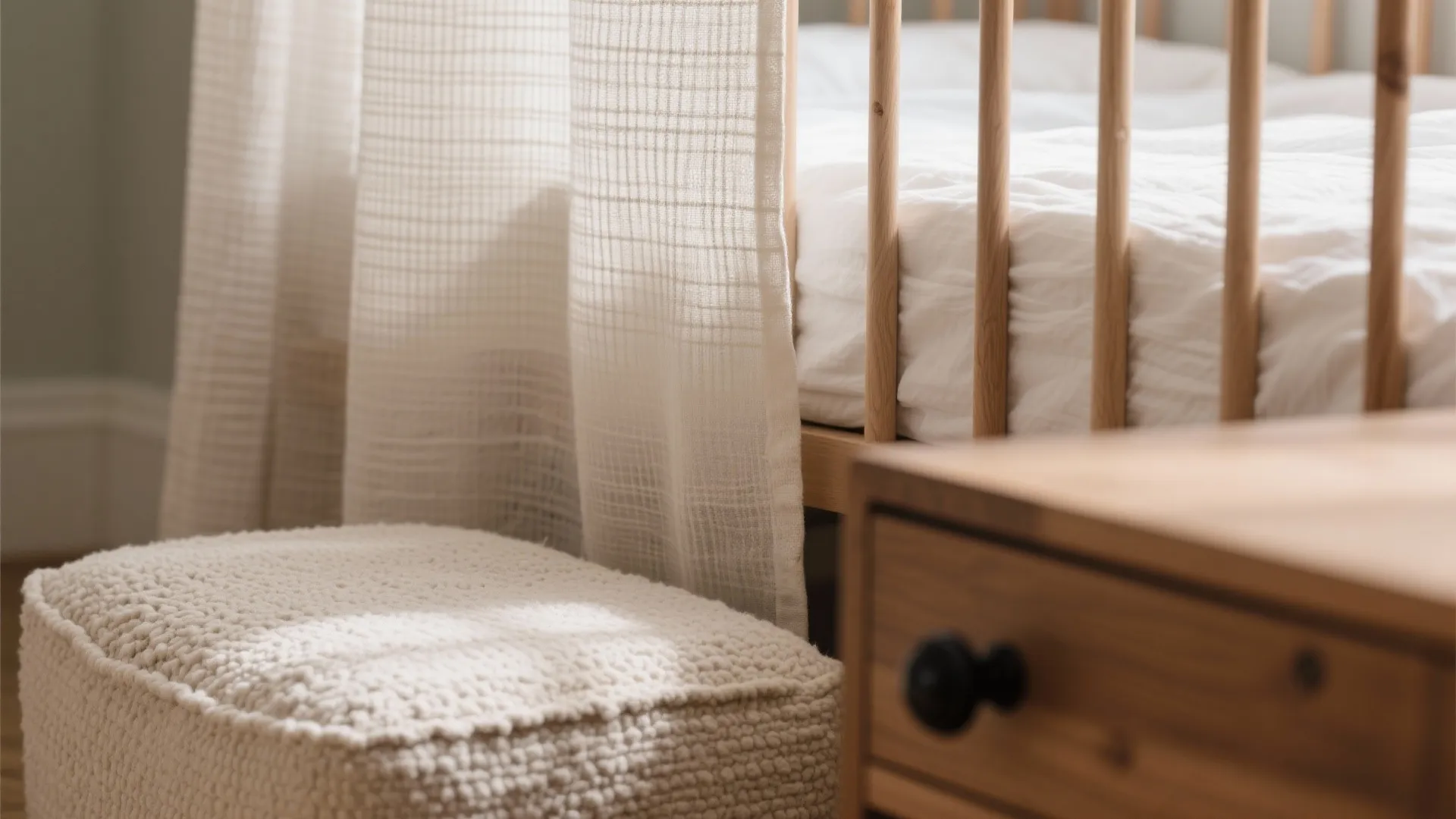 Close up view of a wooden baby bed with white curtains and a soft footrest