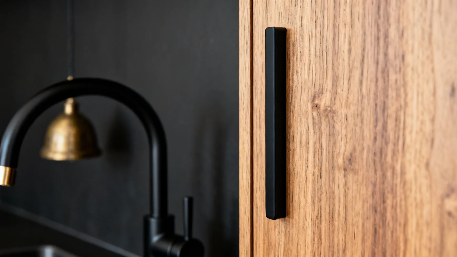 Macro of oak cabinet with matte black pull and brass pendant in background