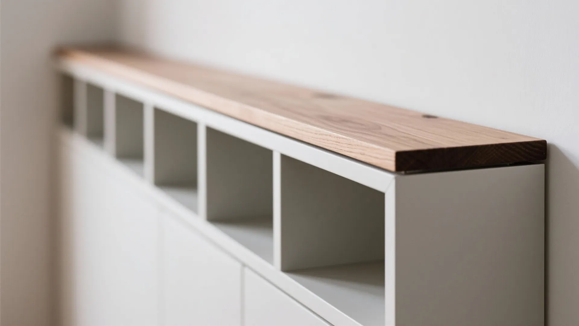 Close-up of a white cabinet with a wooden top and square storage compartments against wall