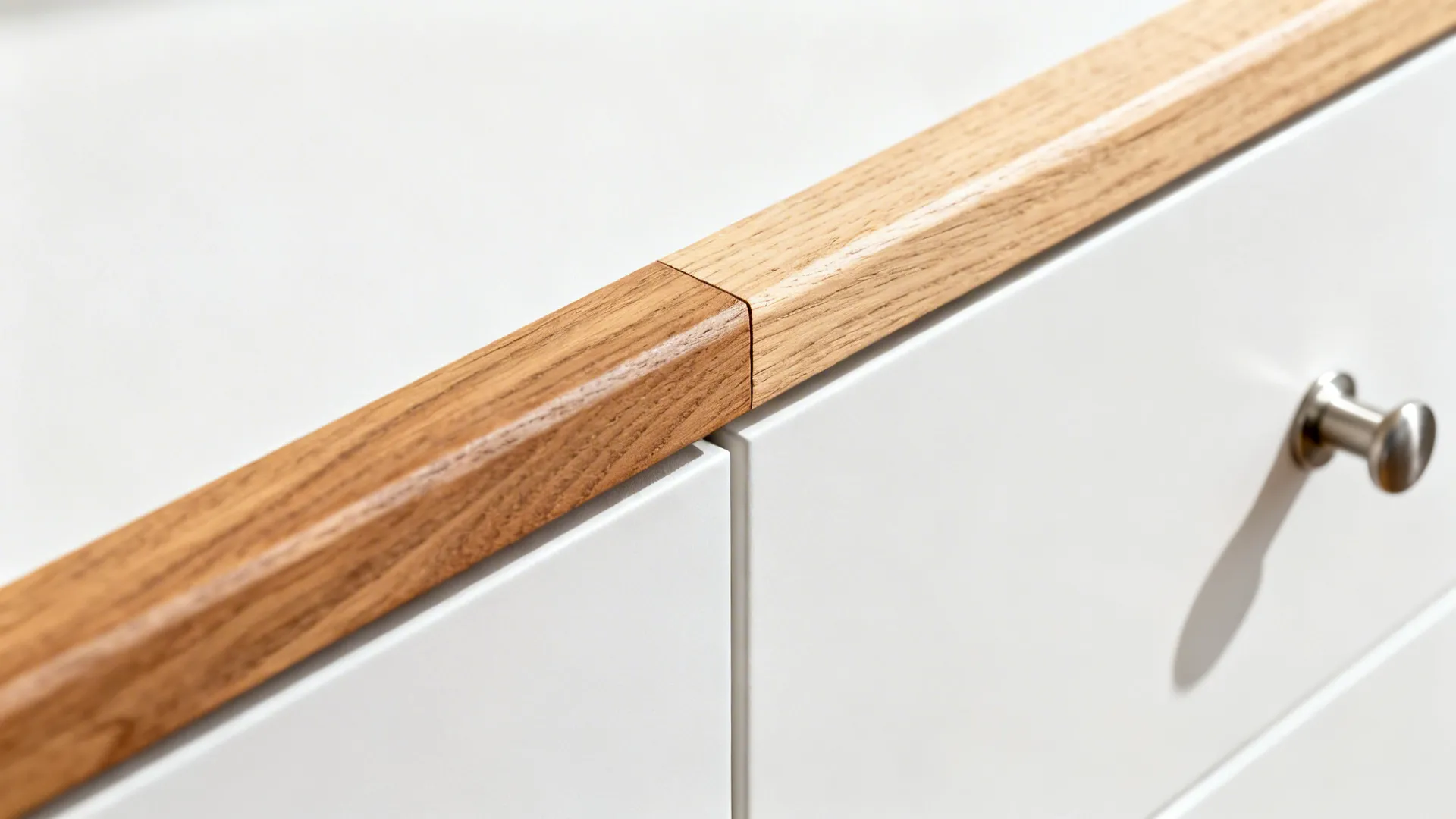 Close-up of a rift-cut oak rail meeting a matte white cabinet with a brushed nickel pull.
