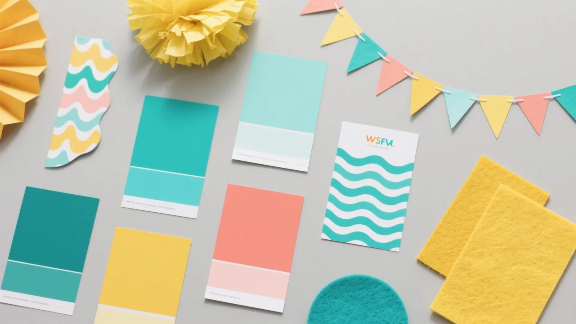 Top-down flat lay of teal, aqua, coral, and sunshine yellow swatches with wave decals and paper-fin garland for a shark-themed party.