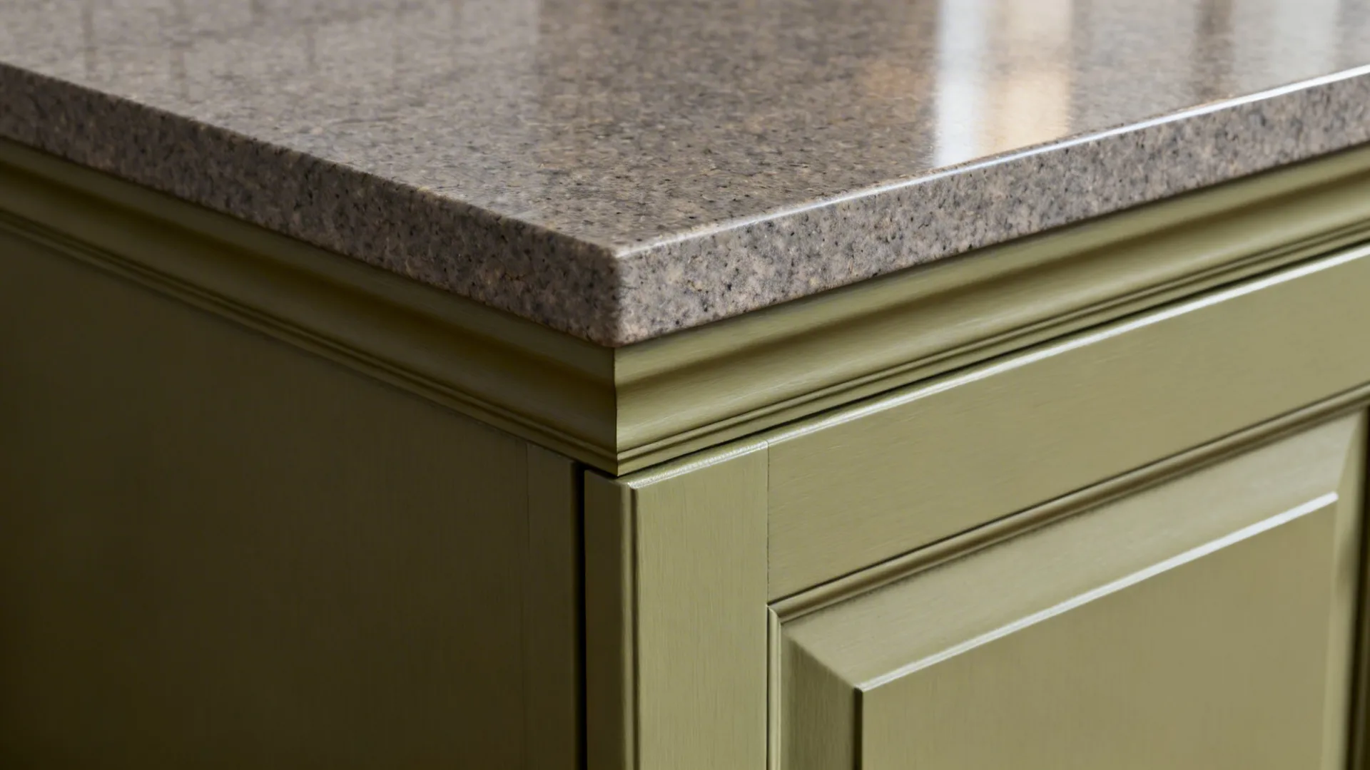 Close-up of a grey stone countertop edge on an olive green cabinet with decorative trim