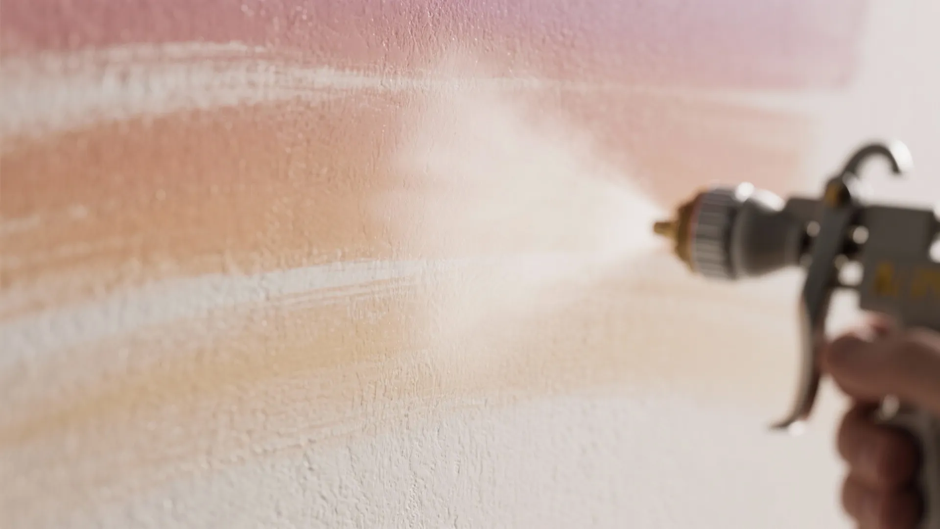 Close up of paint sprayer applying pink and orange gradient color onto a textured wall