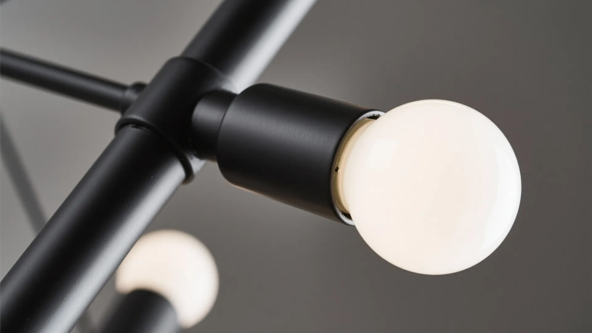 Macro detail of matte black chandelier arm with frosted globe bulb