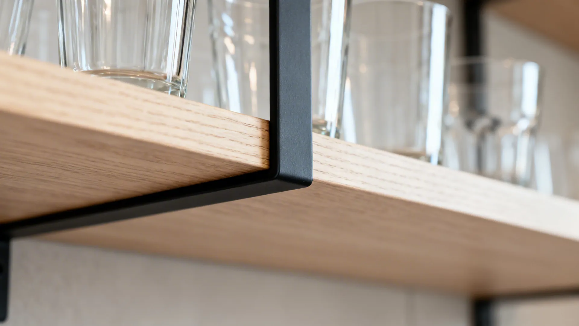 Close-up of light wood shelf with slim black bracket and neatly arranged glass tumblers.