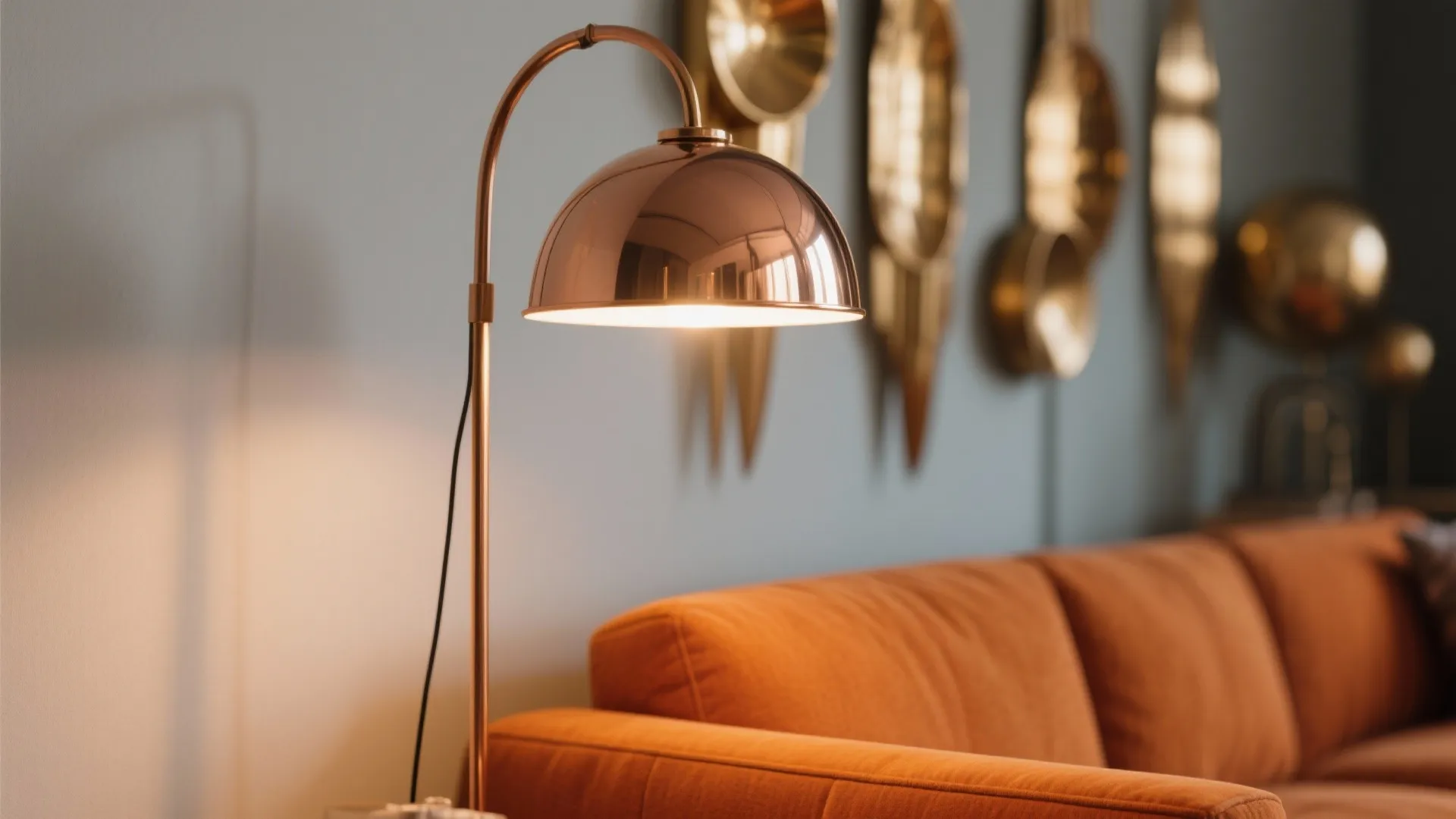 Close up of a copper floor lamp standing next to a modern orange fabric sofa
