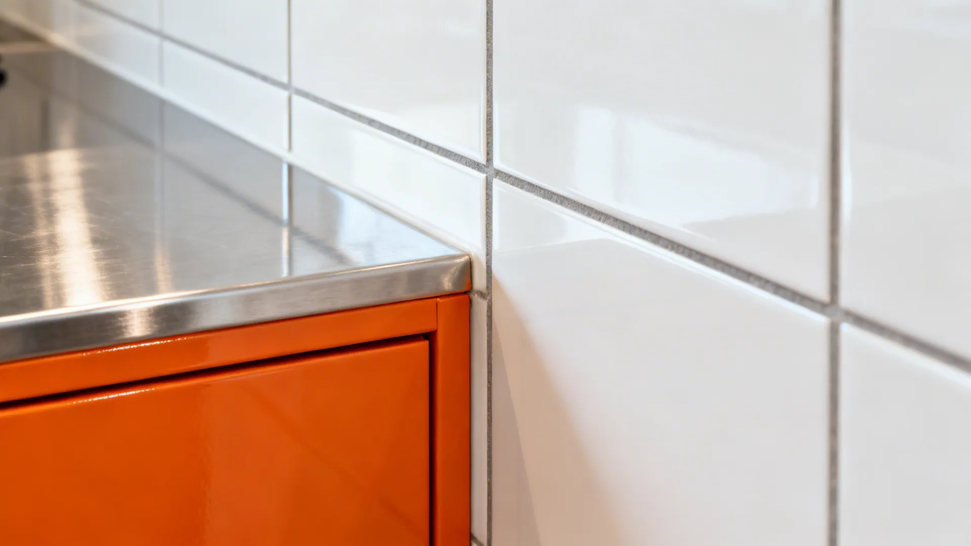 Macro of glossy orange cabinet beside stainless steel and white tile, showing undertone balance.
